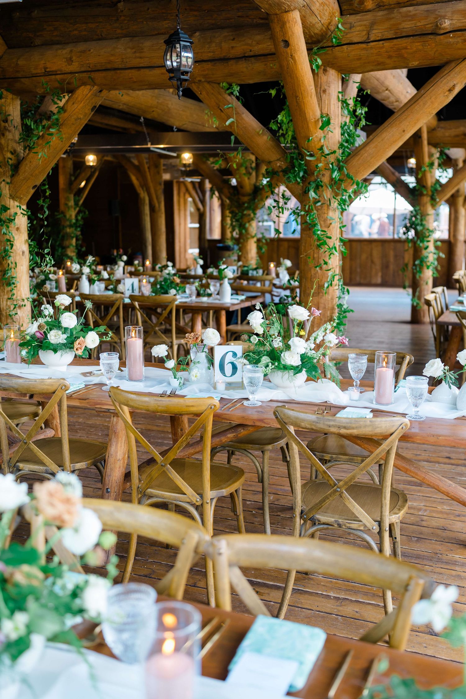 Rustic wedding reception at piney river ranch wedding with wooden beams, floral centerpieces, and cross-back chairs at long tables.