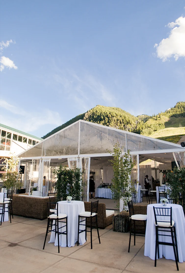 Outdoor wedding reception under clear tent with white tablecloths, chiavari chairs, and mountain backdrop in Aspen.