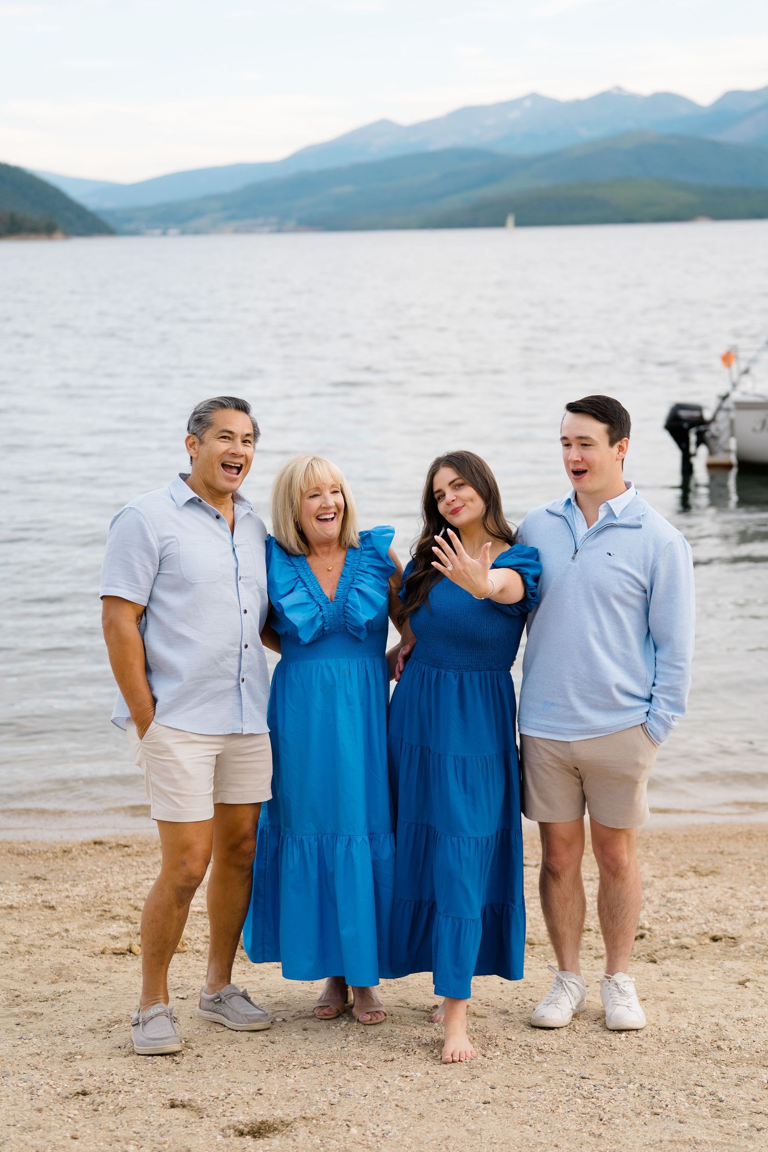 A group in coordinating blue and white outfits laughing together on a beach with mountains and lake in the background at lake dillon marina.