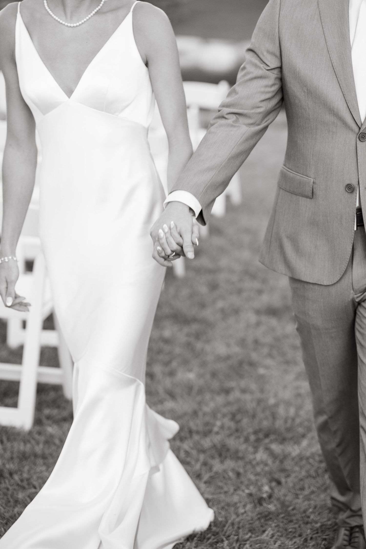 Black and white photo of wedding party members walking on grass with elegant white dresses and gray suits.