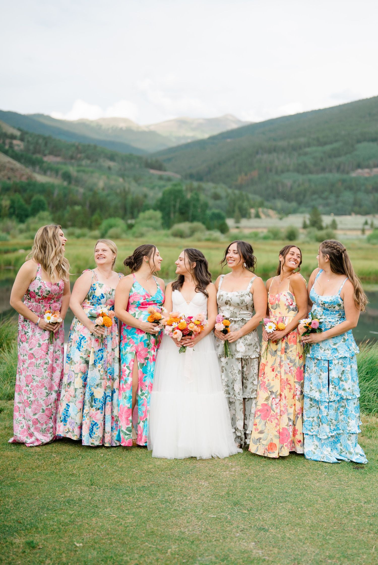 Bridal party wearing vibrant floral maxi dresses standing together in a mountain landscape.