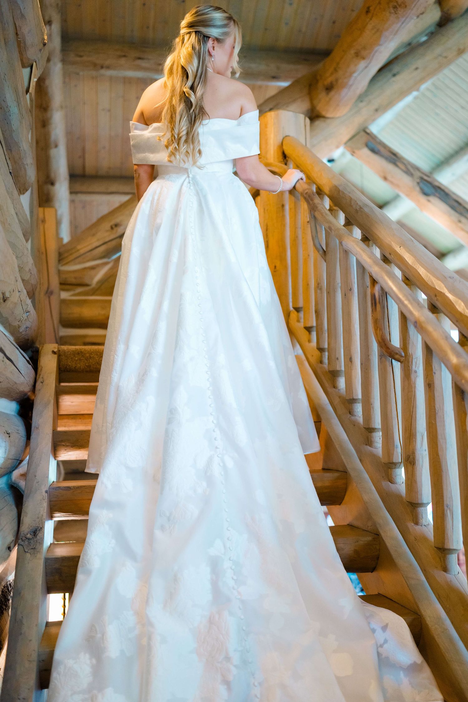 White wedding dress with flowing train cascades down rustic wooden staircase during vail wedding preparation.