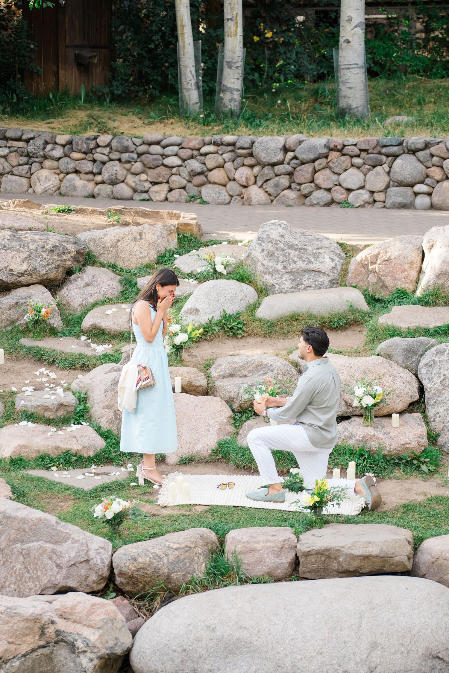 People sit and paint on stone steps surrounded by a natural garden setting with rocks and greenery.