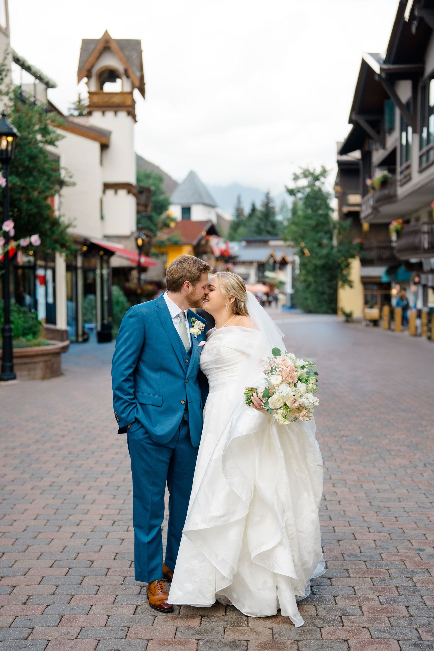 Couple walking on cobblestone street in Vail Village with mountain backdrop during vail wedding.