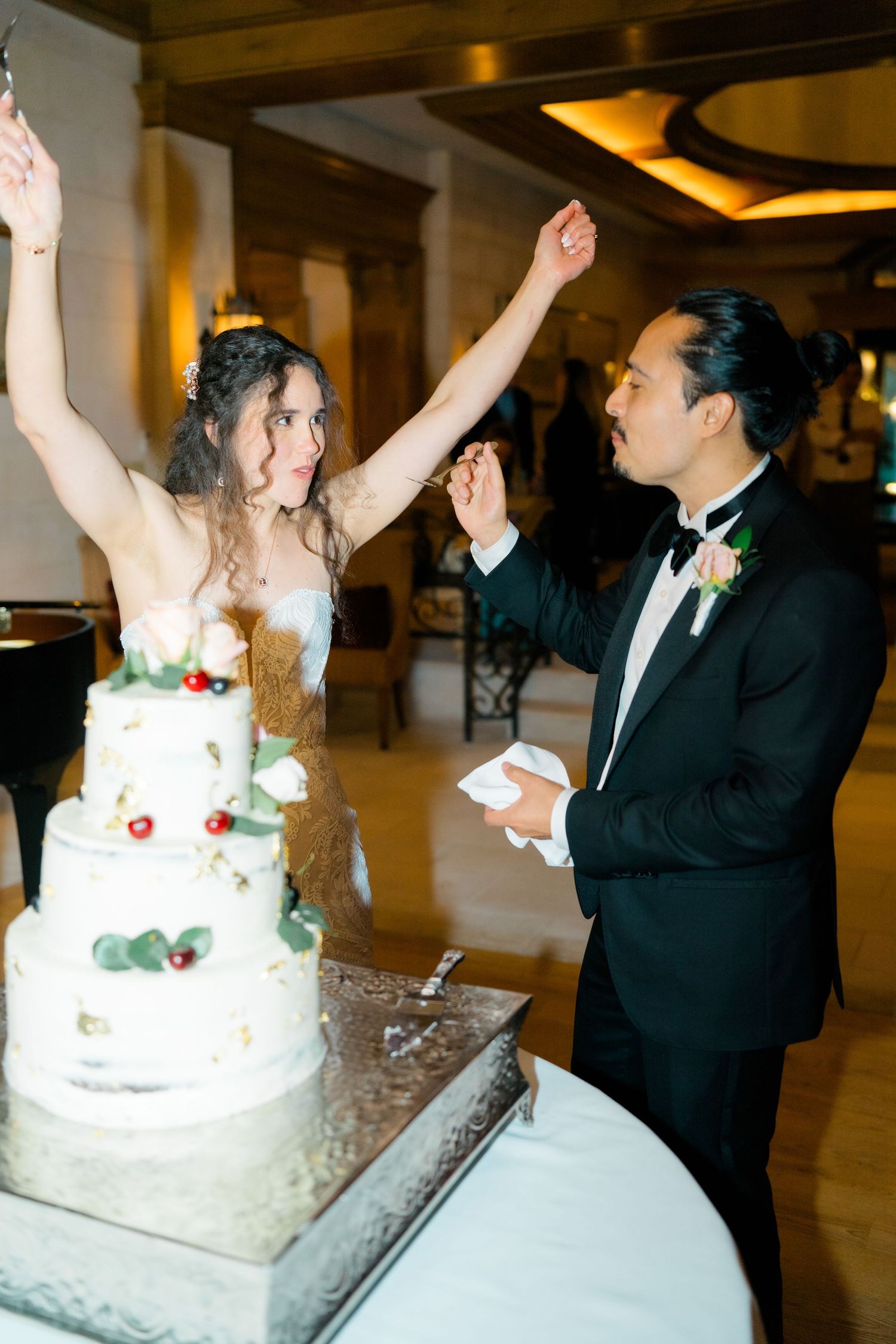 A series of wedding reception photos showing a couple celebrating and raising their arms in joy next to their wedding cake.