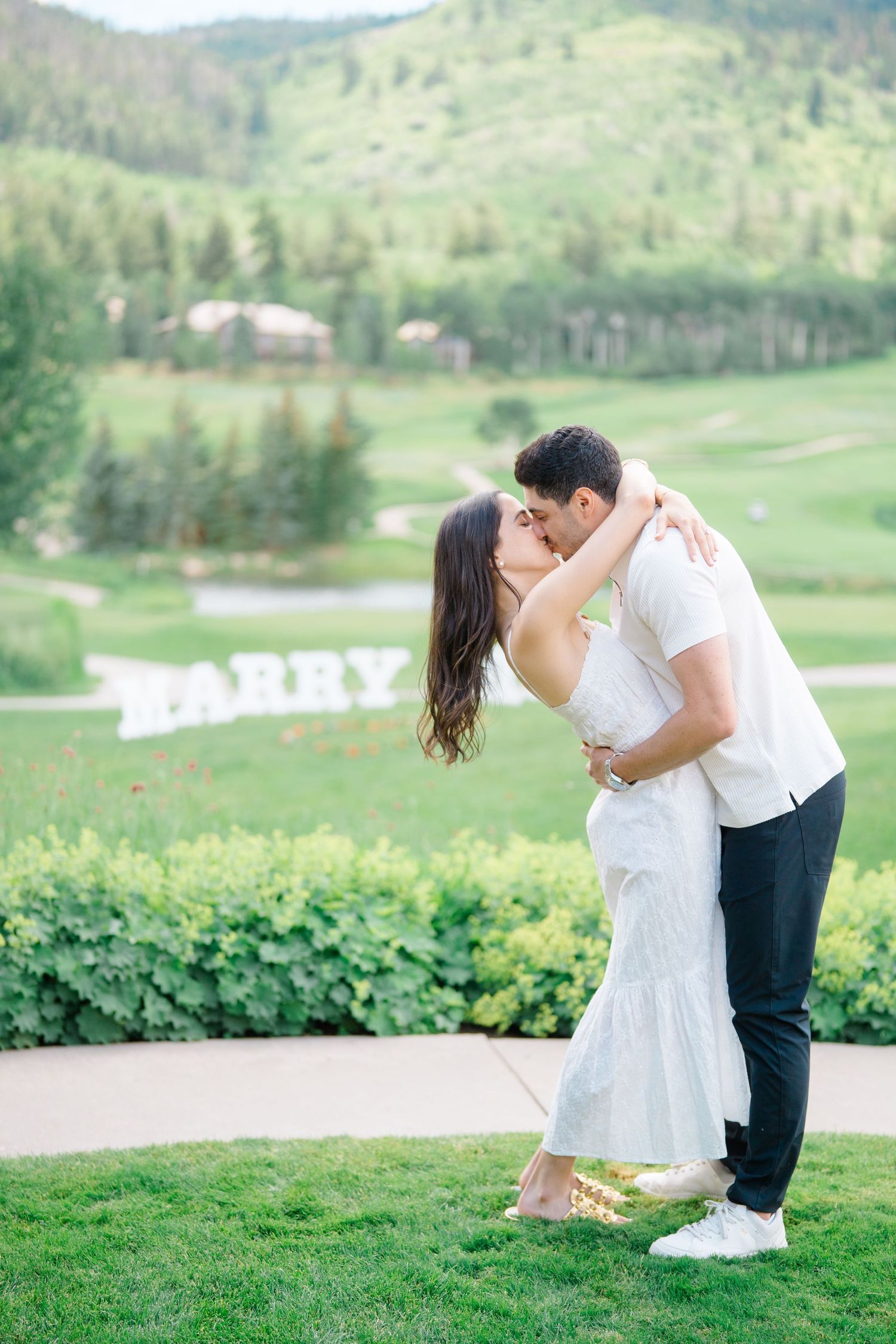 A couple shares an intimate moment on a lush green golf course surrounded by mountain views.