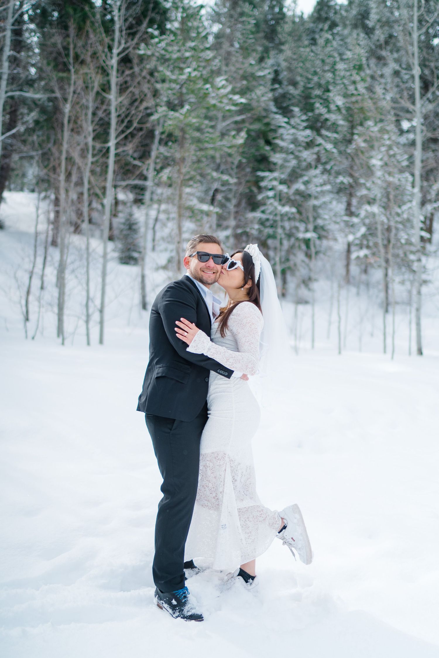 A romantic winter wedding photo series showing a couple embracing in a snow-covered forest setting.