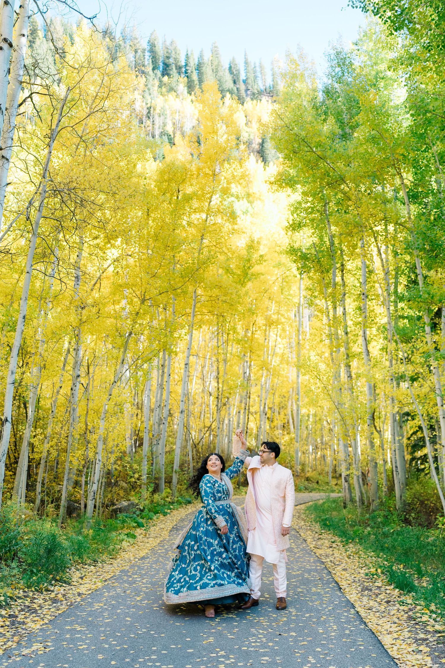 Two people walk along a scenic autumn path surrounded by golden aspen trees in a forest setting.