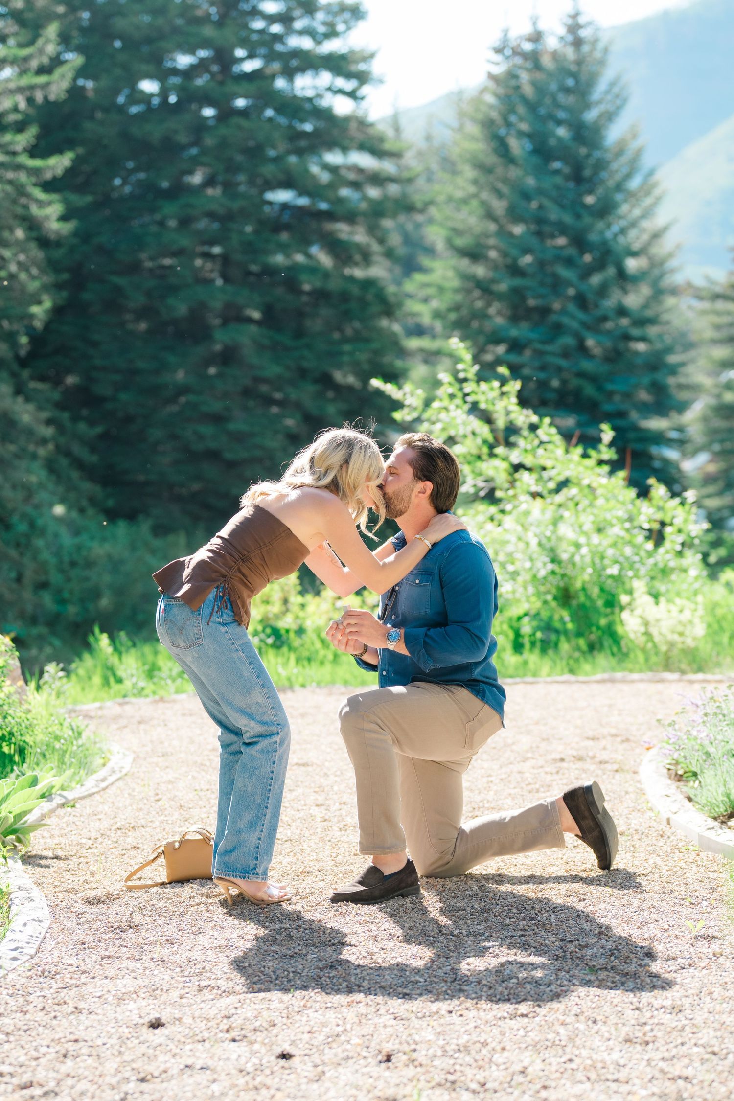 A romantic proposal sequence captured in a mountain setting with evergreen trees and natural scenery in the background.