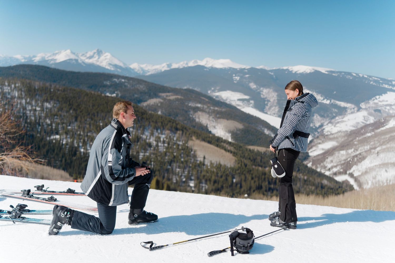 Panoramic view of snow-covered mountain peaks and vail ski slopes on a clear winter day with skiers enjoying the terrain during proposal.