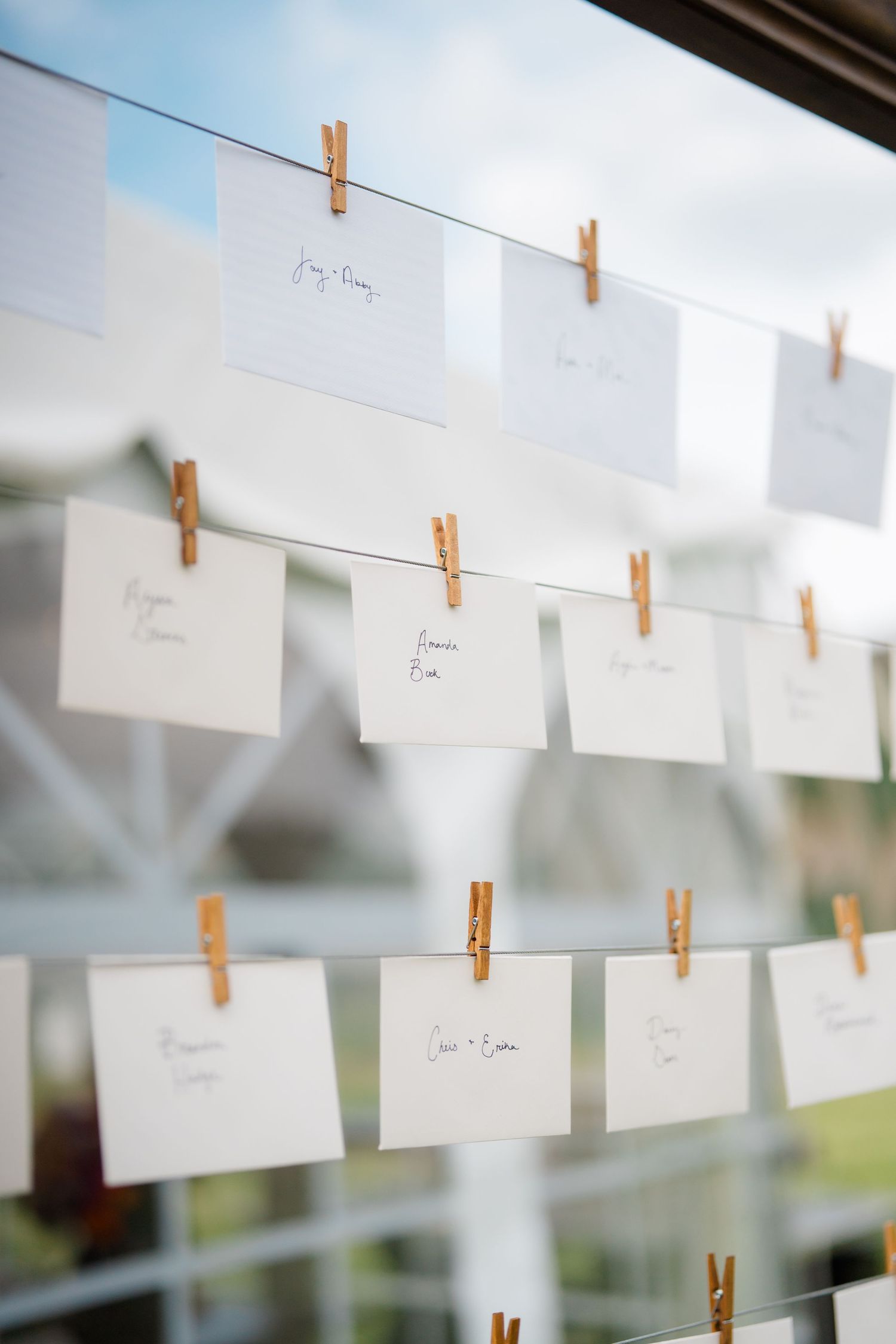 White name cards hung with wooden clothespins on string lines for wedding seating.