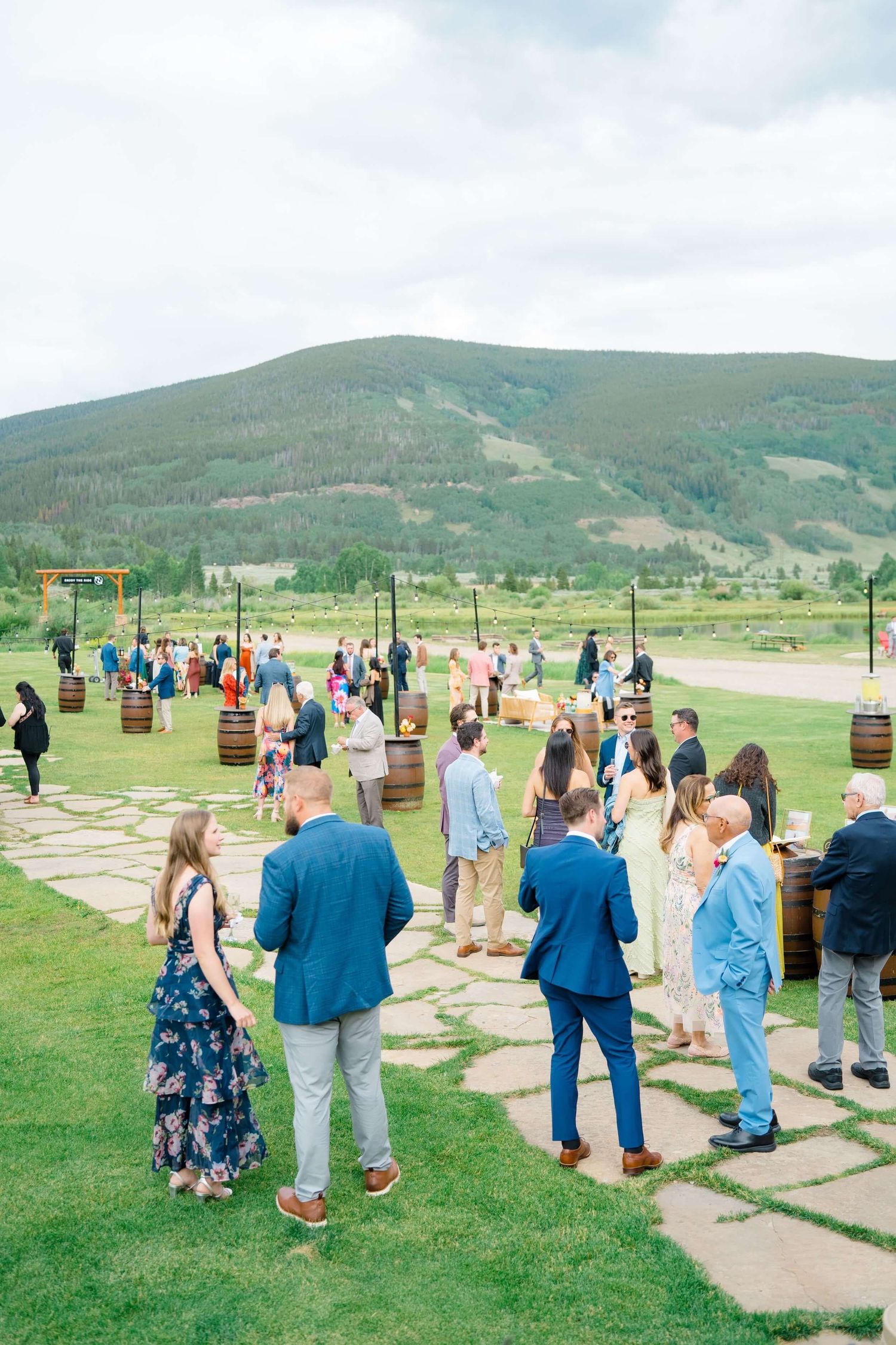 Camp Hale Wedding guests gather on stone pathway at outdoor mountain venue with green hills in background.