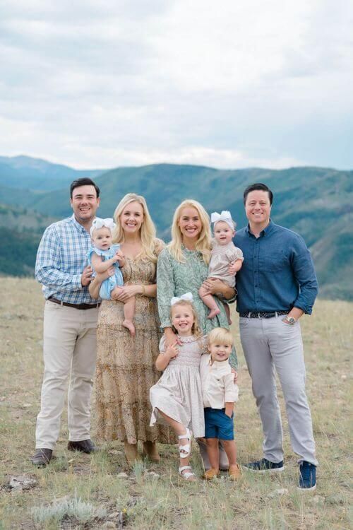 A group in coordinated outfits poses together on a grassy hillside with mountains in the background - vail family photograph locations.