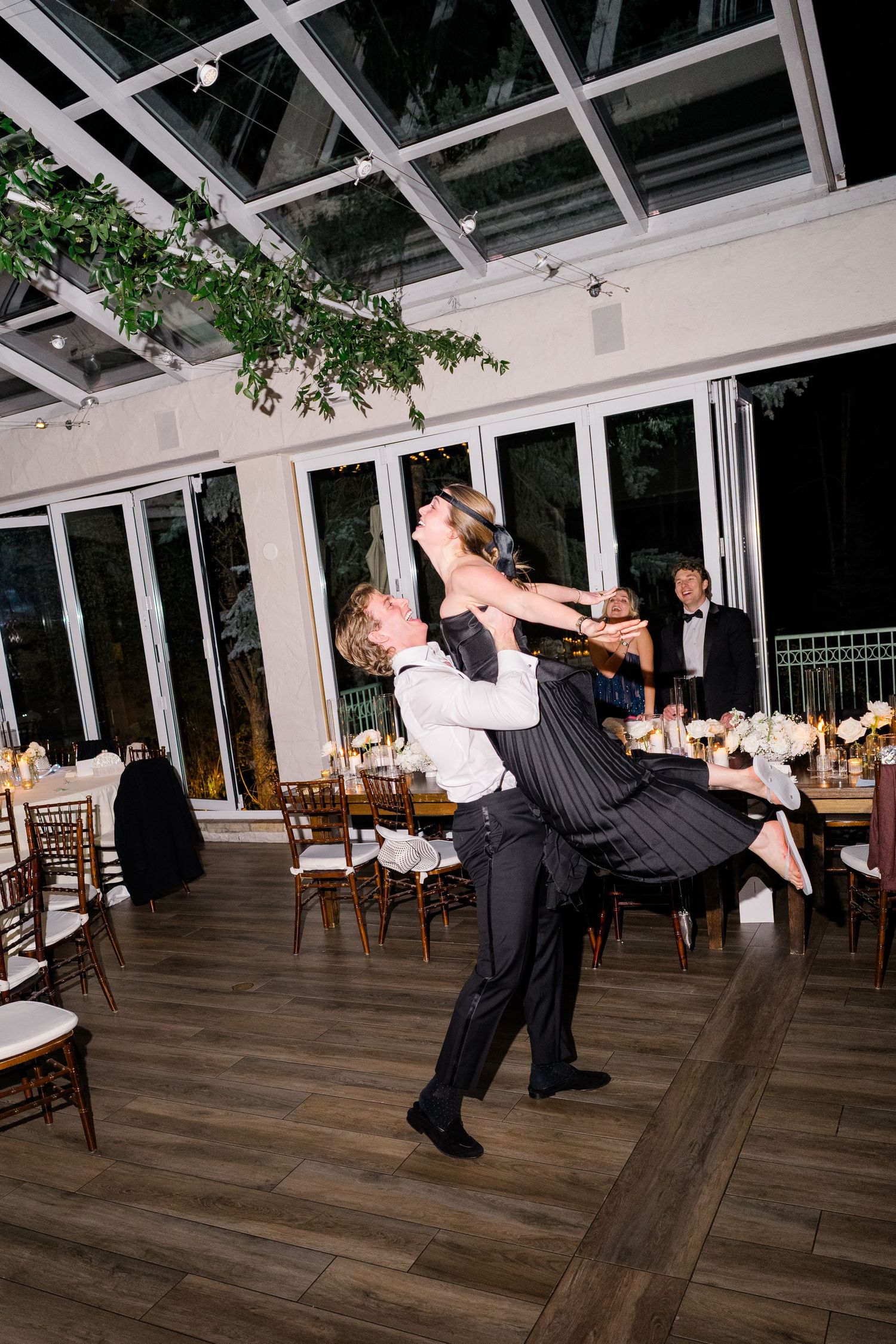 Couple shares an elegant first dance lift in a glass-walled ballroom with candlelit tables and lush greenery overhead at Vail Sonnenalp.