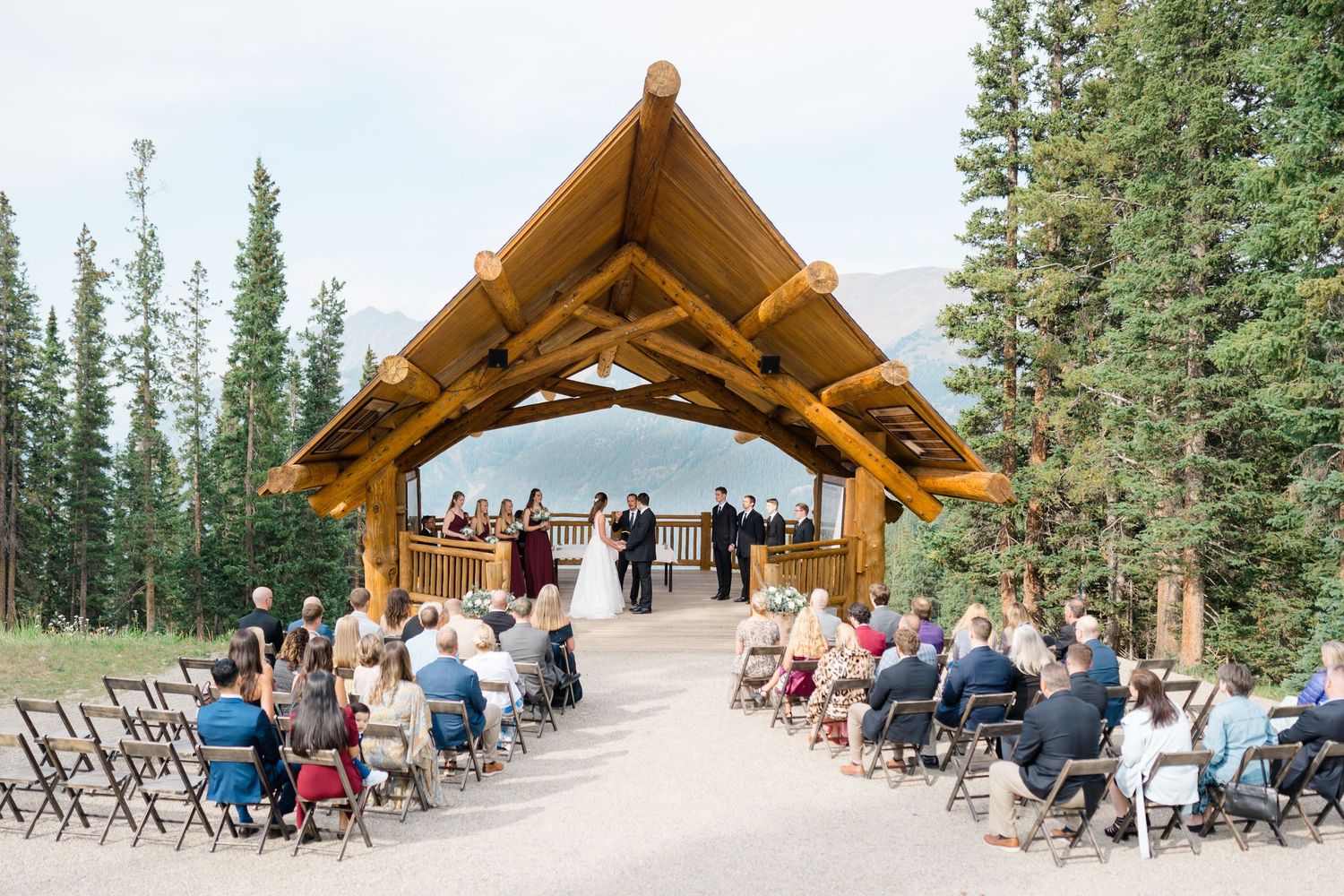 Outdoor mountain wedding ceremony setup with wooden pavilion and chairs surrounded by evergreen trees at copper mountain.