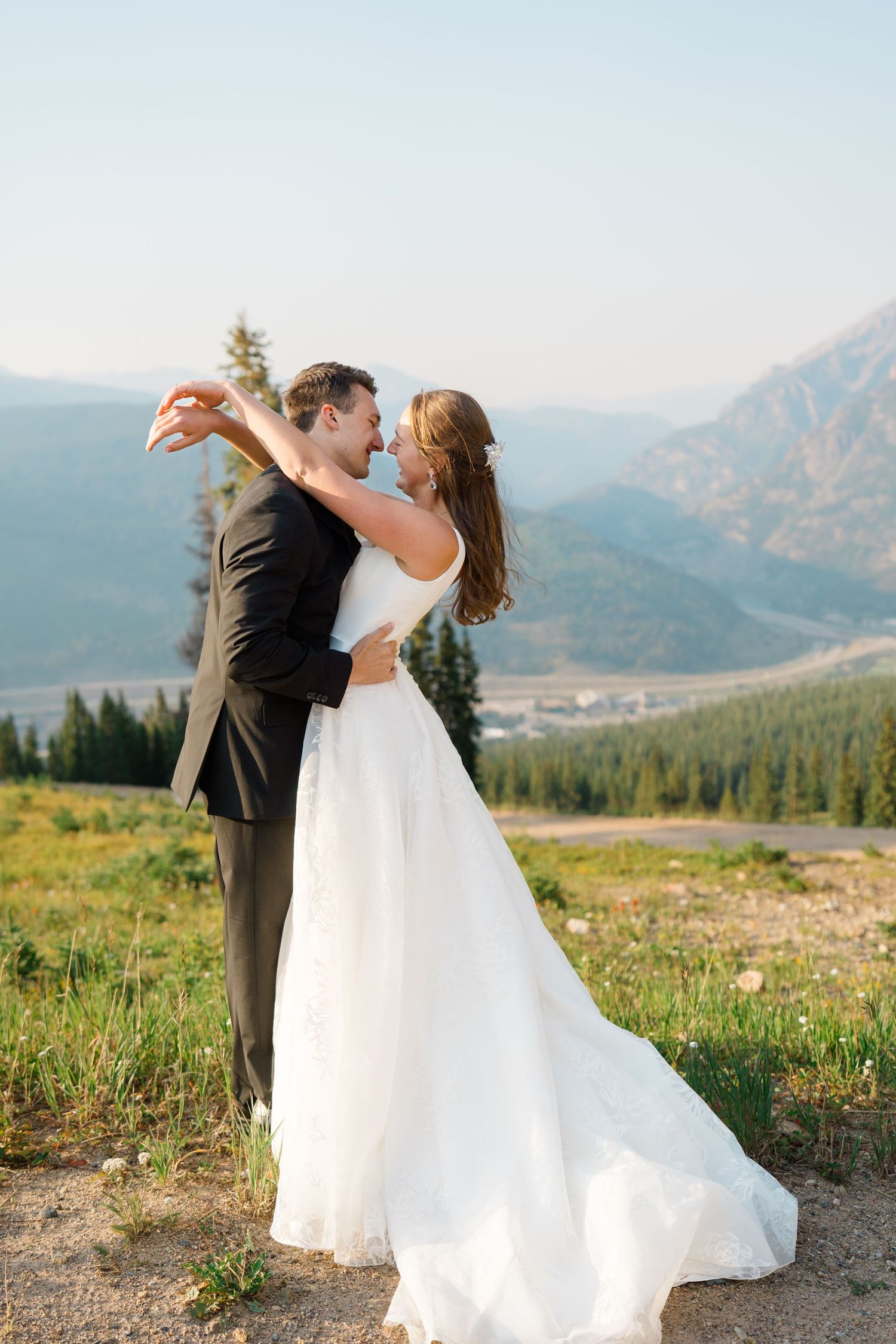 A couple in wedding attire dances together on a scenic mountain meadow at copper mountain with dramatic mountain peaks in the background.