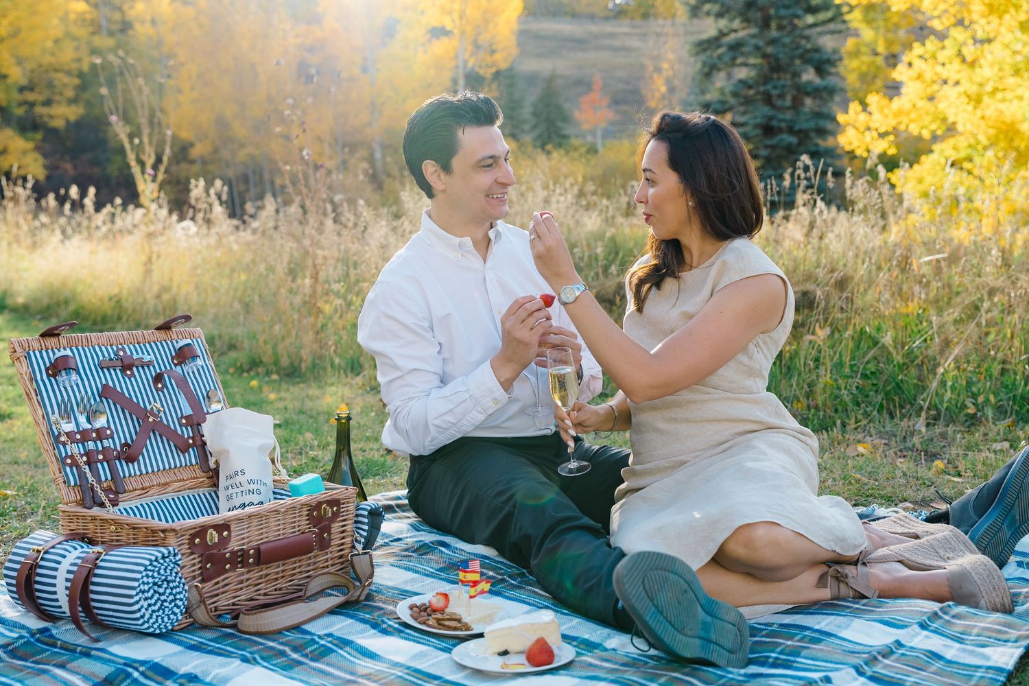 Couple enjoying a romantic sunset picnic on a blanket surrounded by golden autumn foliage and wildflowers during vail proposal session.