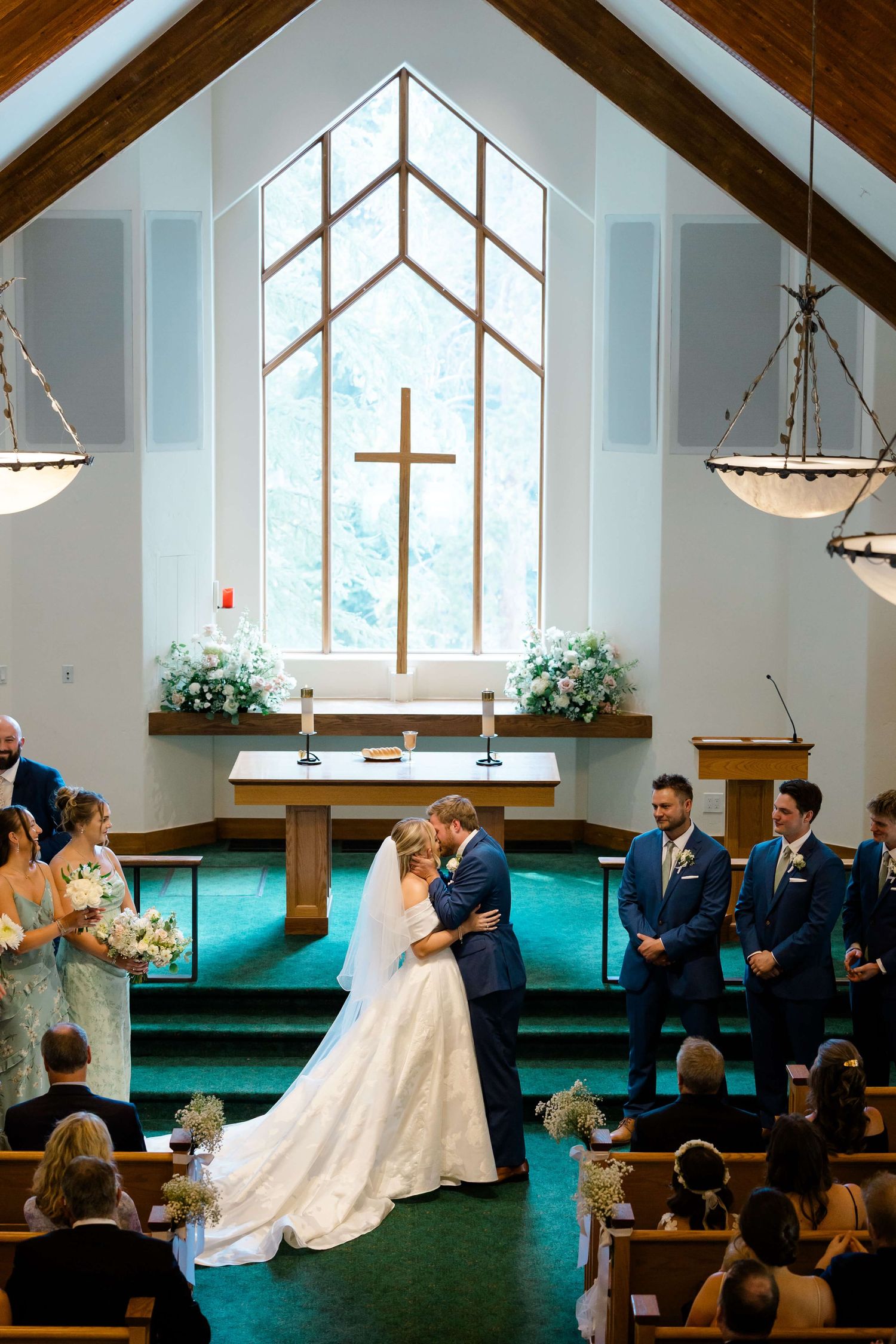 A wedding ceremony takes place in a church with dramatic vaulted ceilings and hanging chandeliers during vail wedding.