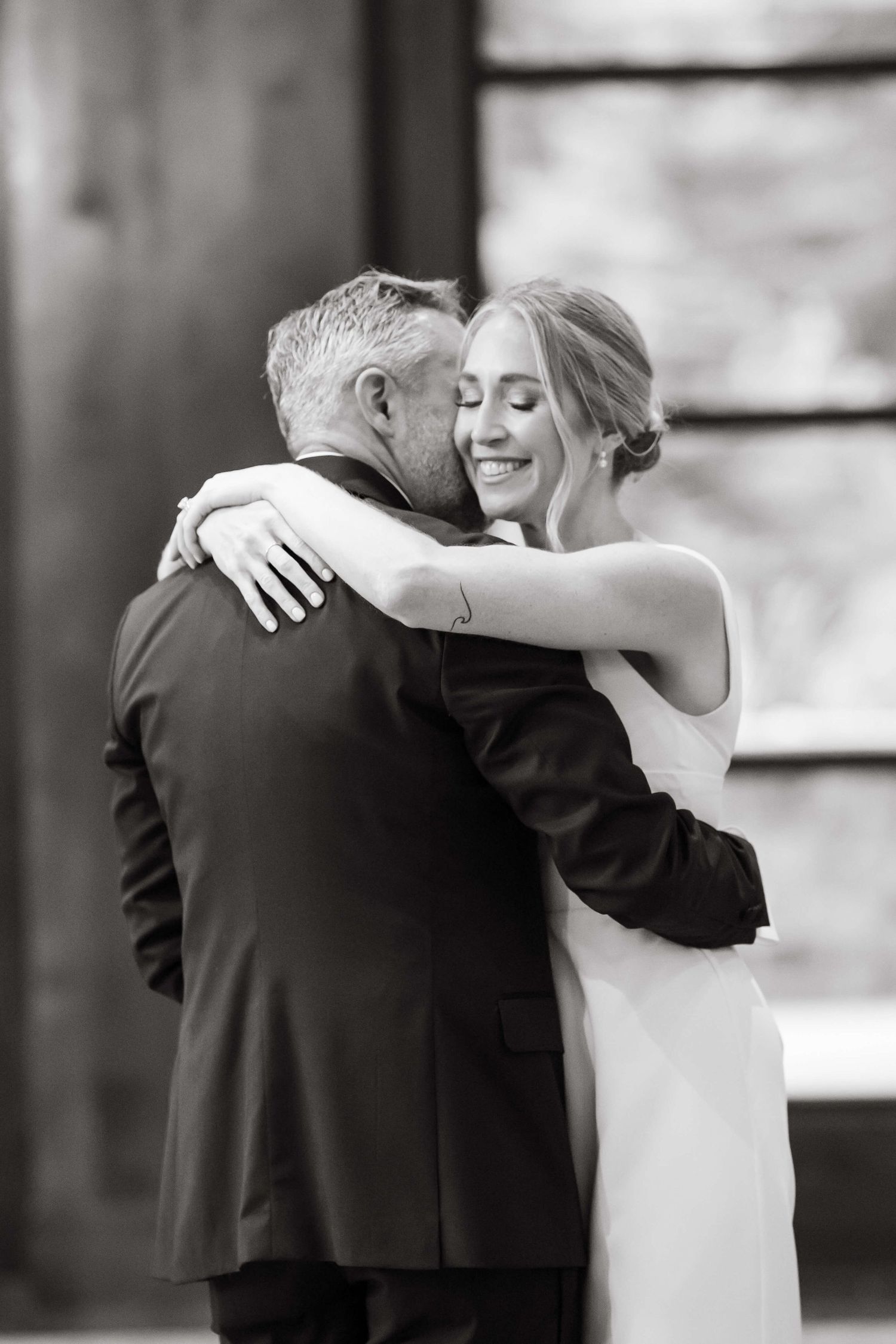 At Vail Golf Club Wedding Venue - Black and white photo of a bride smiling while embracing her groom in a tender wedding moment.