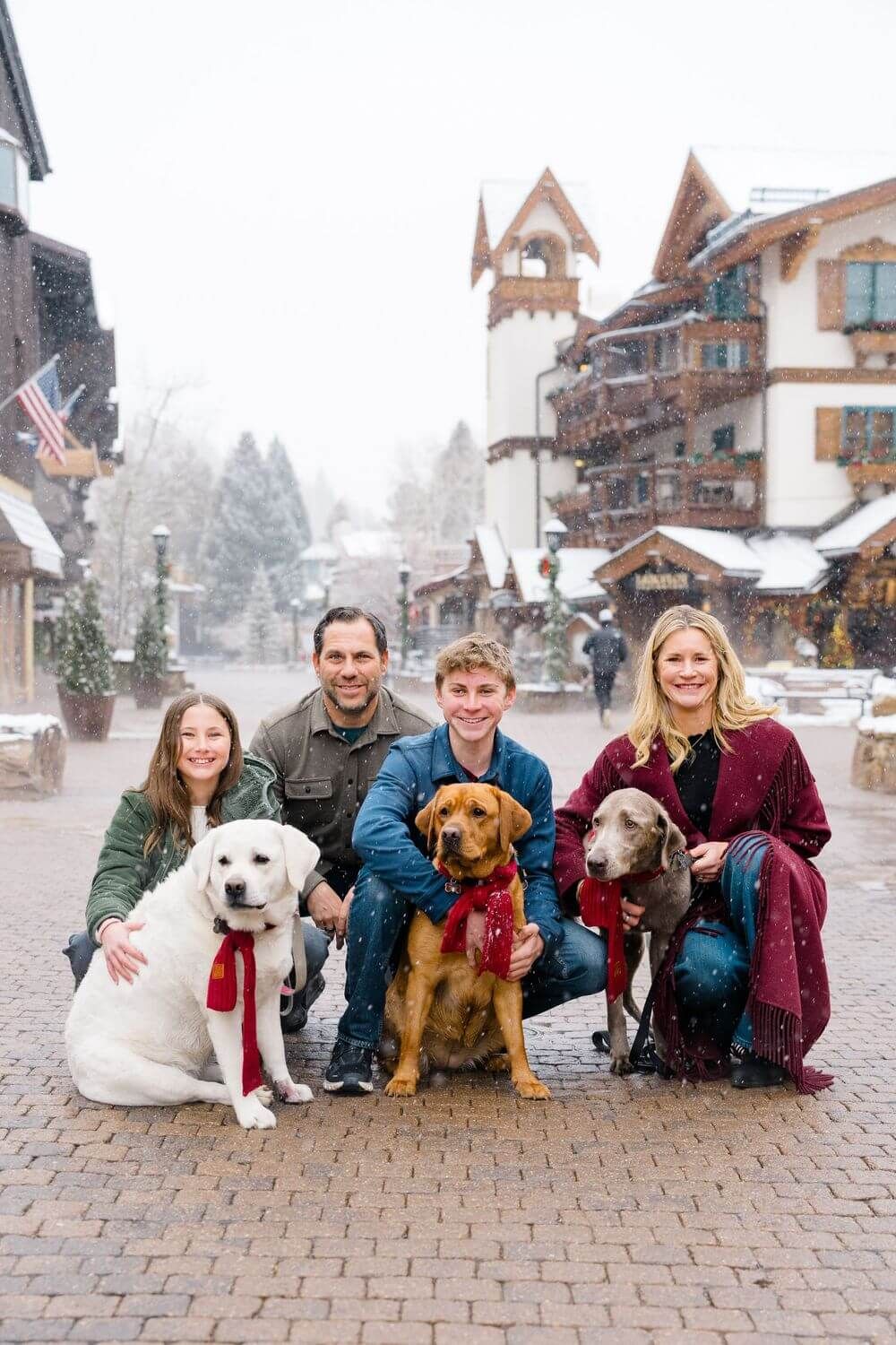 Vail Family Photography best locations - Family and their dogs posing together on a snowy cobblestone street in front of winter chalets.