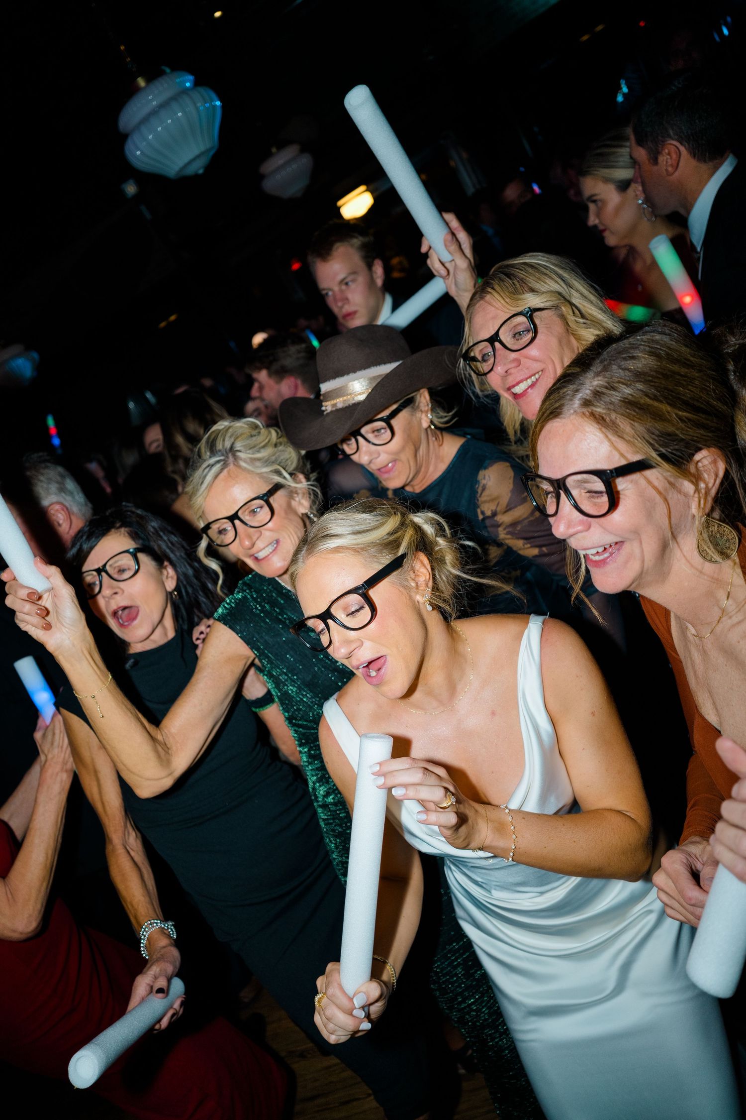 Party guests wearing novelty glasses dance and celebrate at a nighttime event.