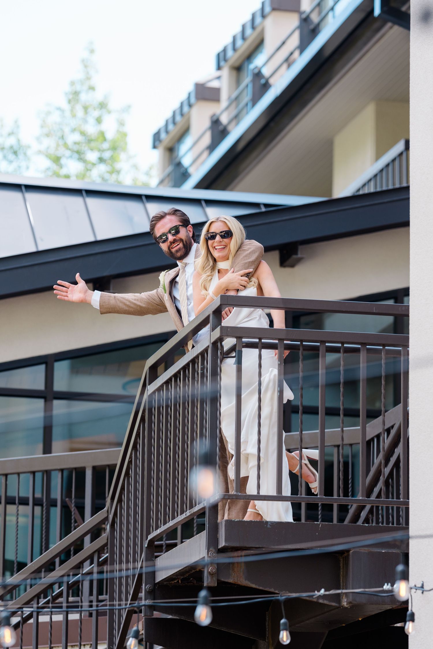 Stylish couple in sunglasses smiling on modern building staircase outdoor balcony on a sunny day.