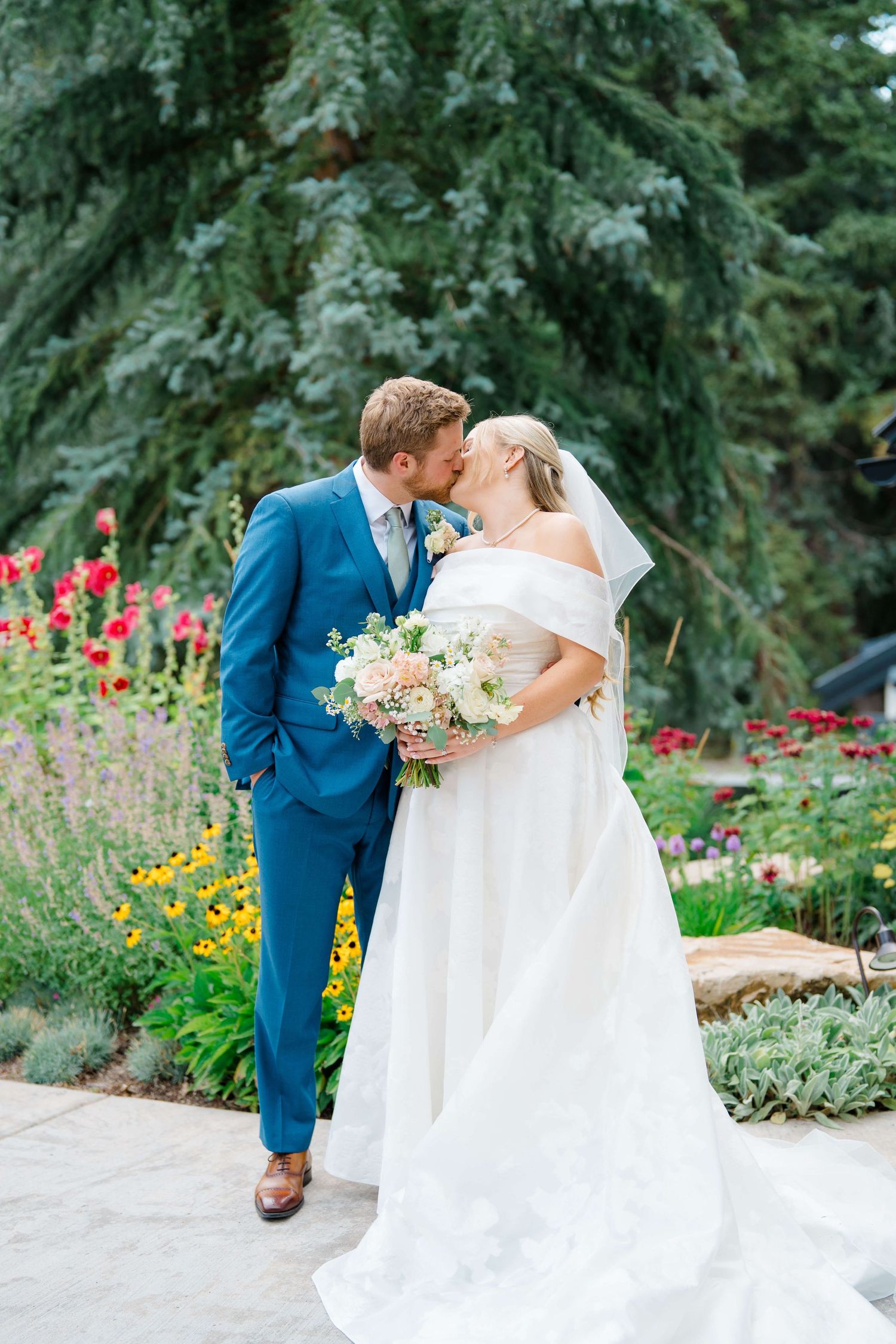 A romantic wedding portrait in a garden with evergreen trees and colorful flowers in bloom during vail wedding.