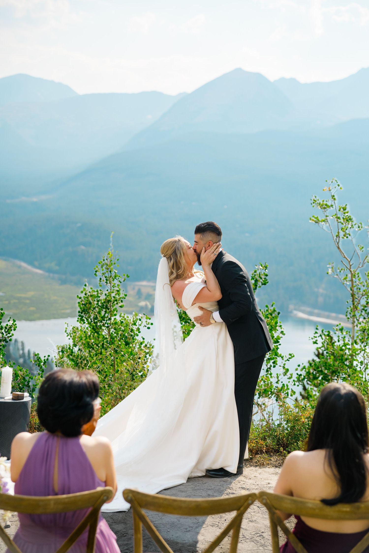 A couple shares a romantic moment during their mountain wedding ceremony overlooking a scenic lake vista.