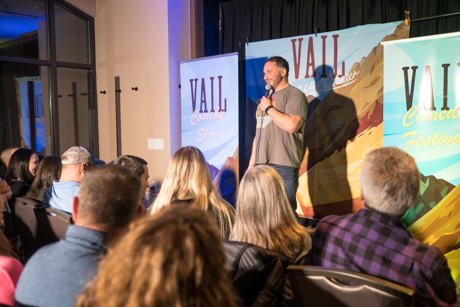 An audience watches a performer on stage with a scenic mountain backdrop display.
