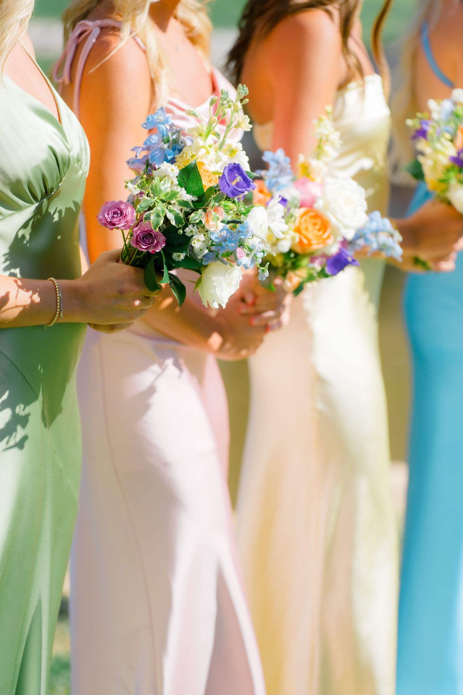 Bridesmaids hold colorful spring bouquets while wearing pastel mint and turquoise dresses at an elegant wedding ceremony.