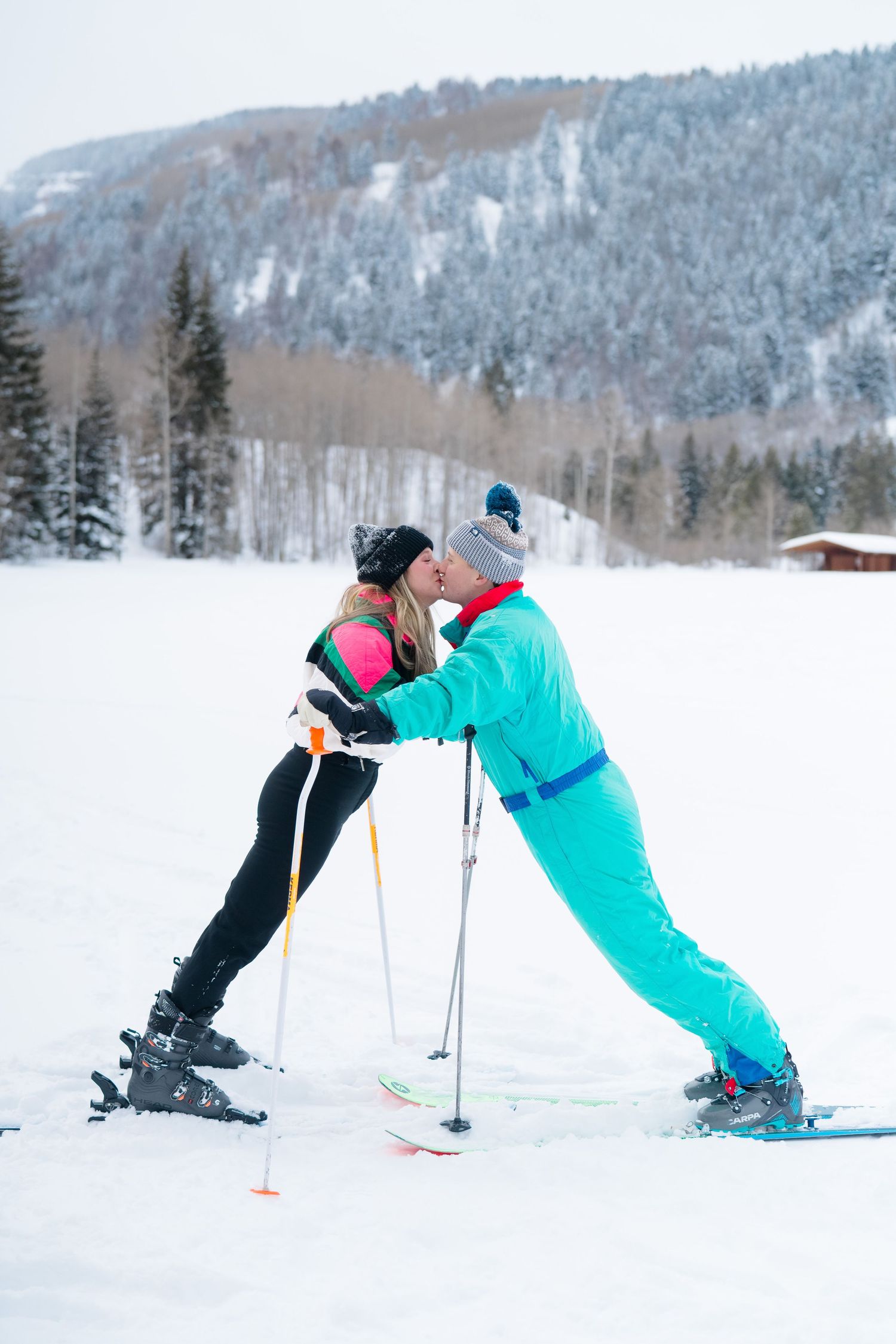 guy and girl kissing for their engagement session on skis looking forwards each other