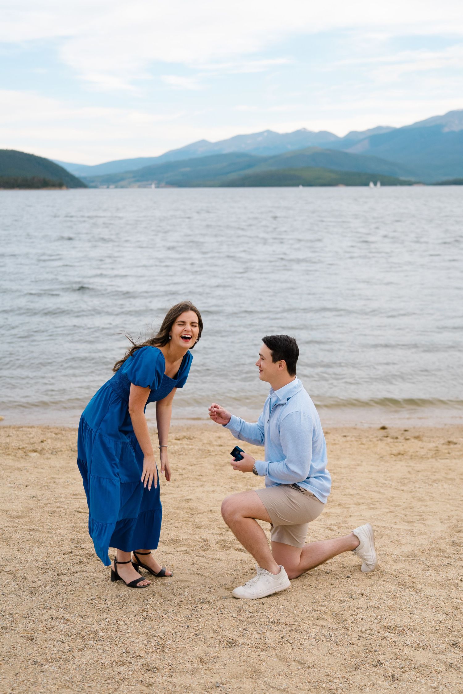 A romantic proposal moment on a sandy beach with mountains and lake in the background.