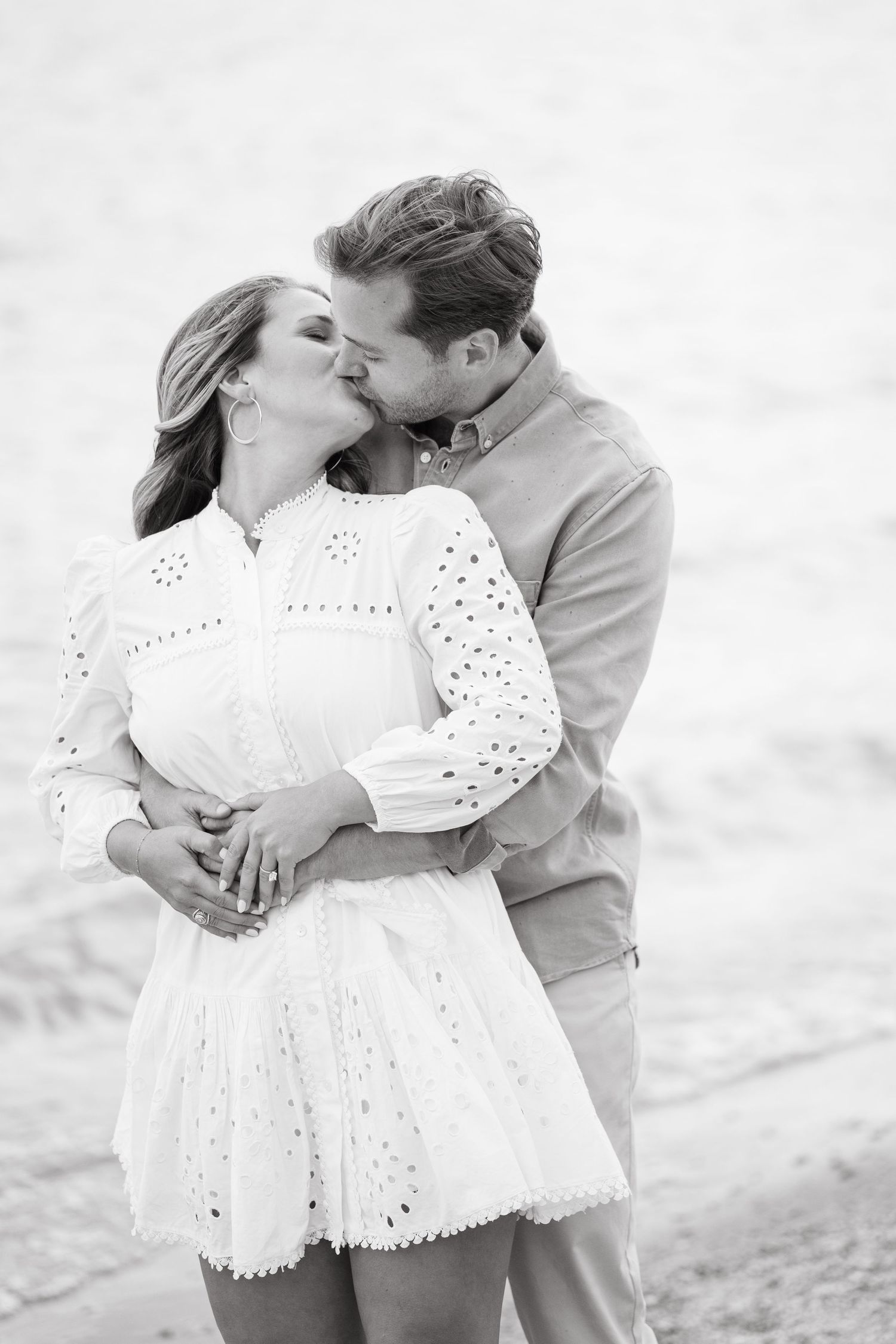 A romantic black and white photo series of a couple embracing on a beach in casual attire.