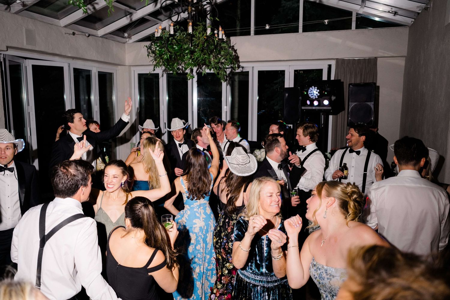 Guests dancing at a lively wedding reception under a chandelier in an elegant venue.