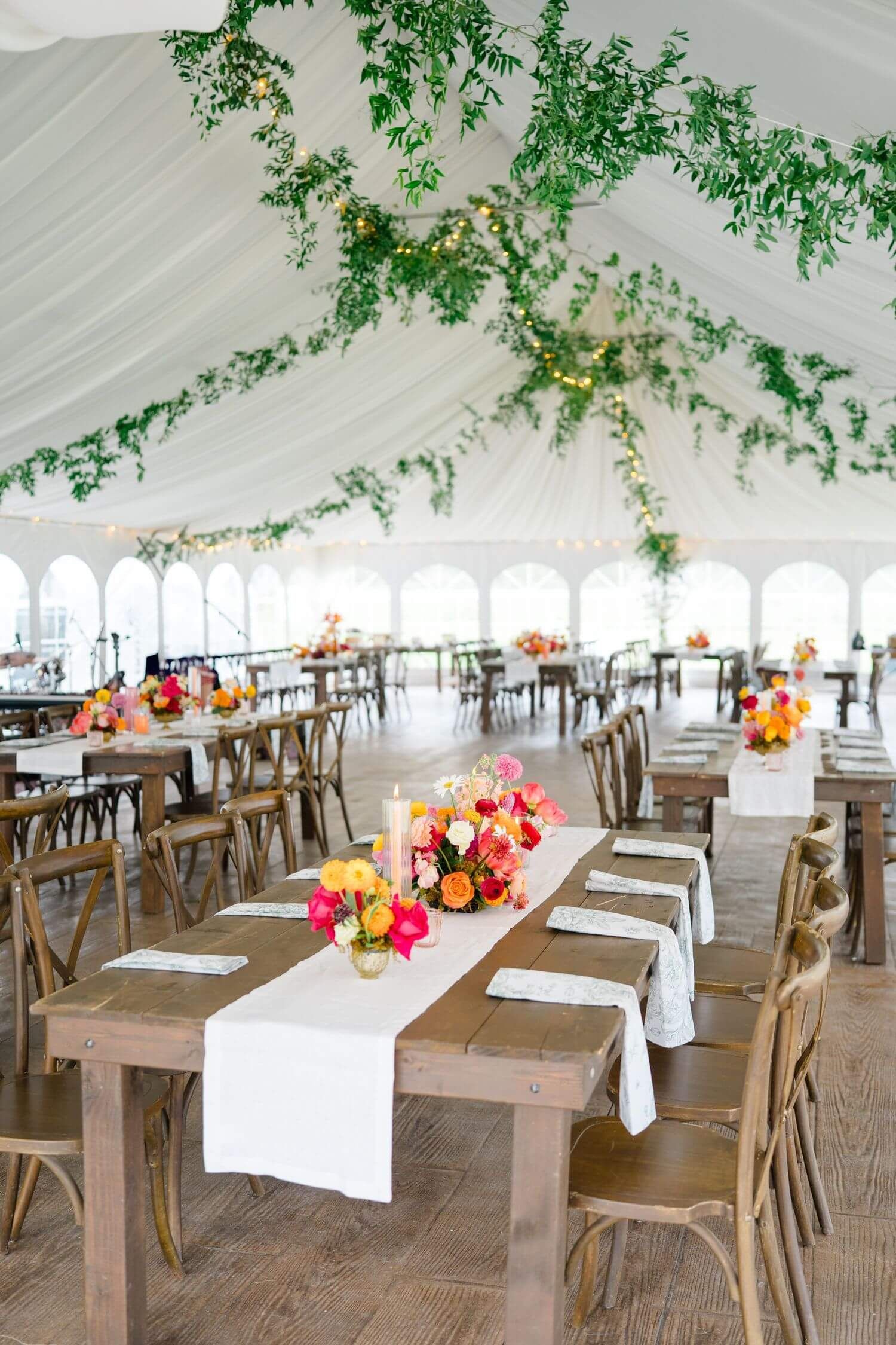 Elegant wedding at camp hale reception tent with draped white fabric, greenery decor, wooden farm tables and colorful floral centerpieces.