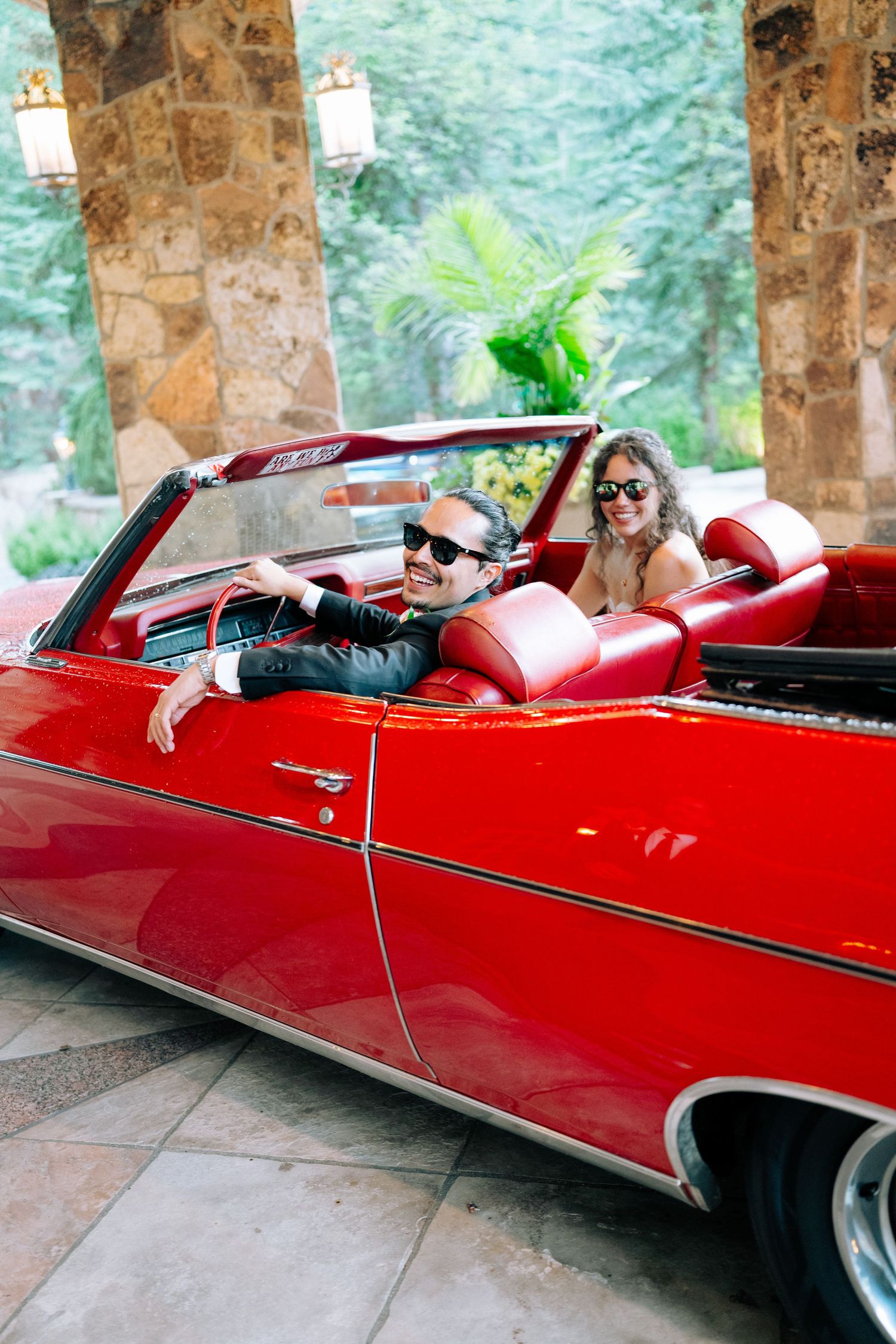 A classic red convertible car with sleek lines parked under a stone archway.