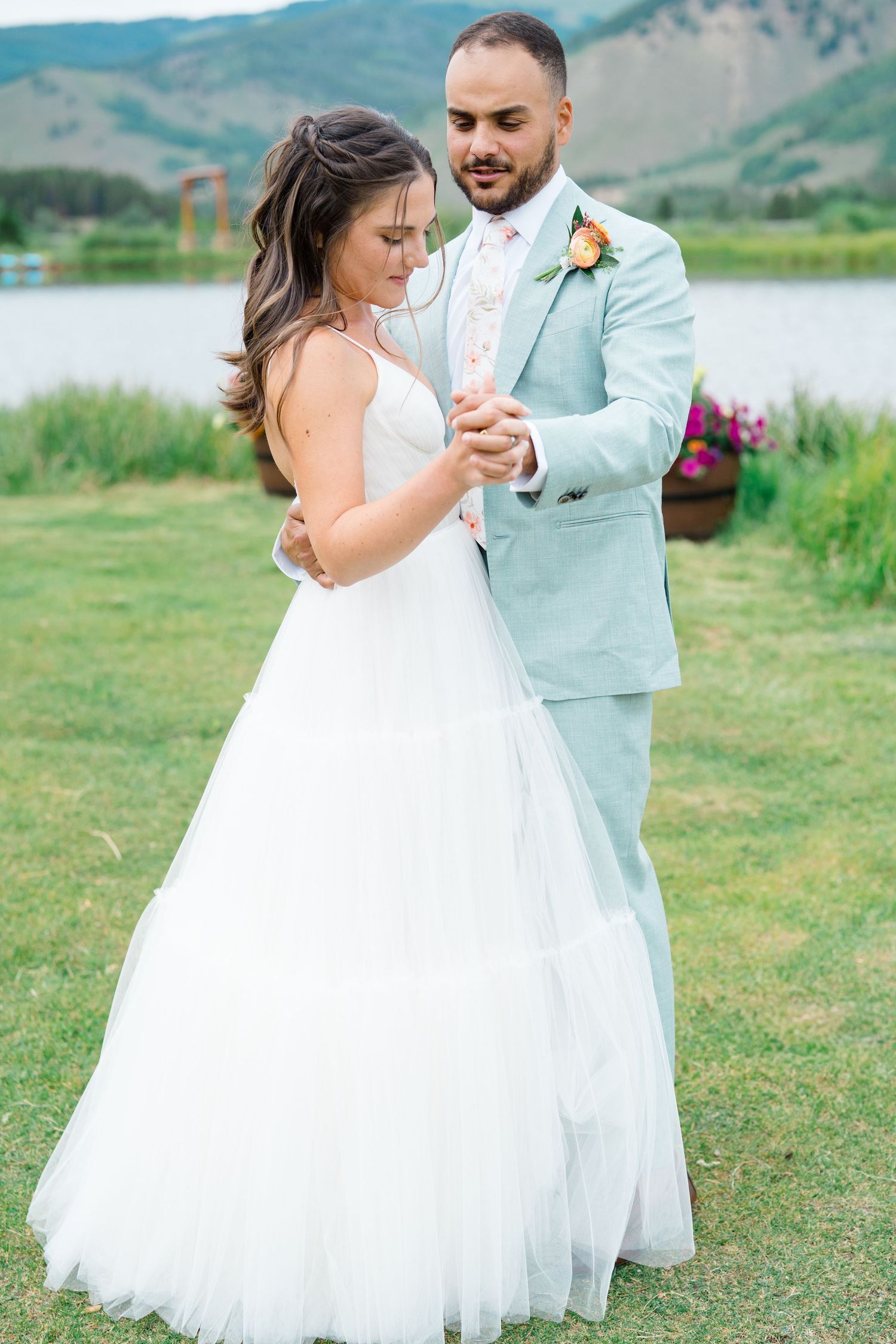A couple dances together on a grassy meadow with mountains in the background during their wedding celebration.