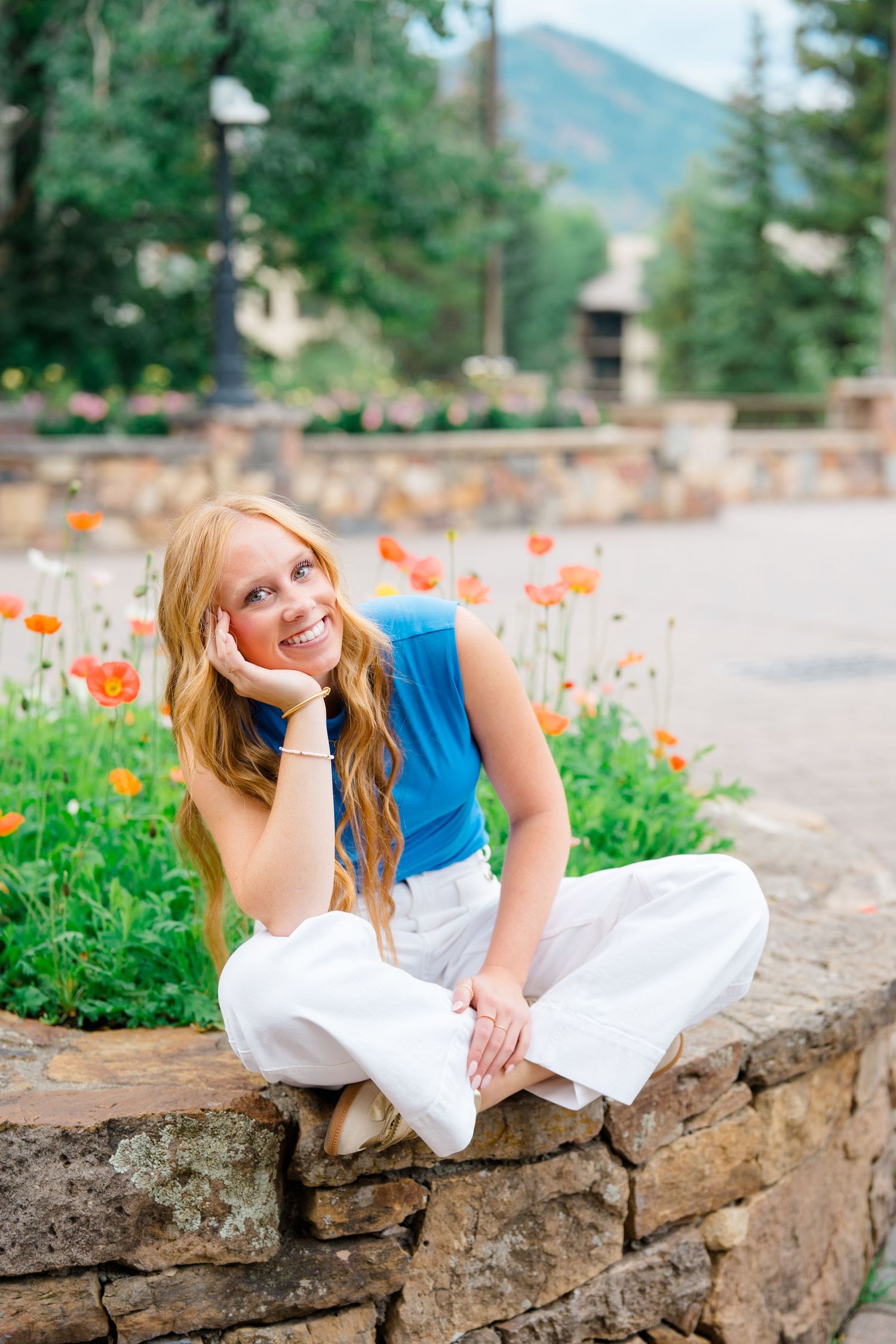 Summer fashion by orange poppies and stone wall with mountains in background during vail senior photography session.