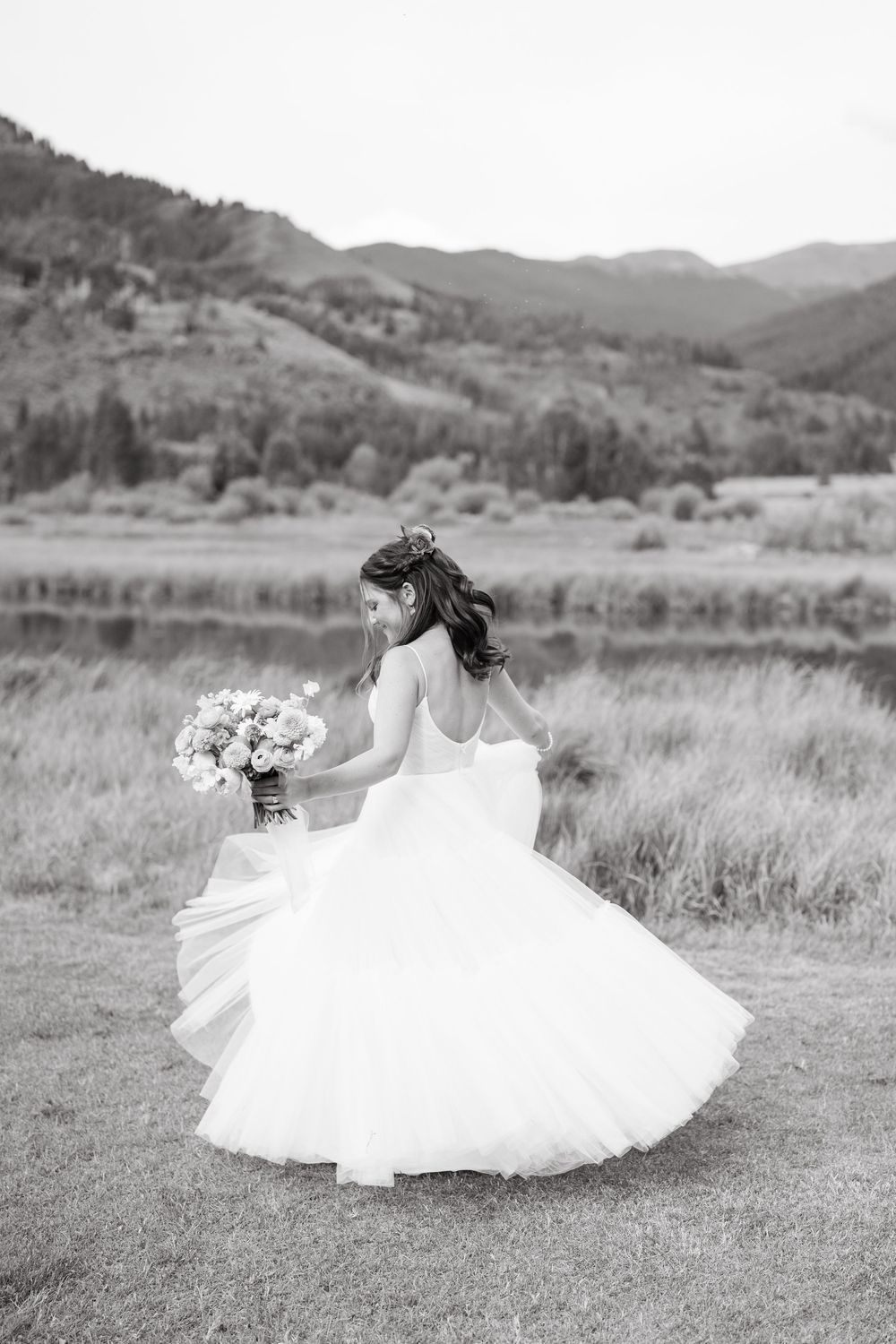 A bride in a flowing white wedding dress twirls joyfully in a scenic mountain meadow setting in vail colorado by vail wedding photographer.