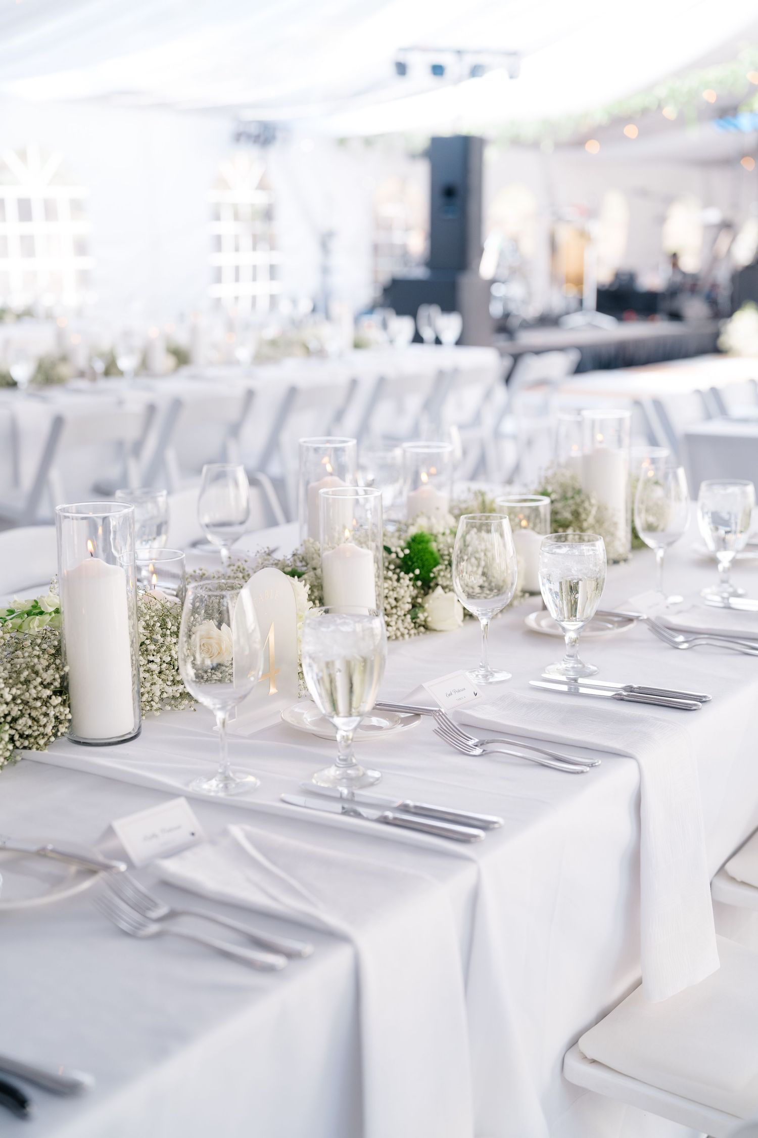 Elegant white wedding reception table with candles, baby's breath, crystal glassware, and white linen tablecloth.