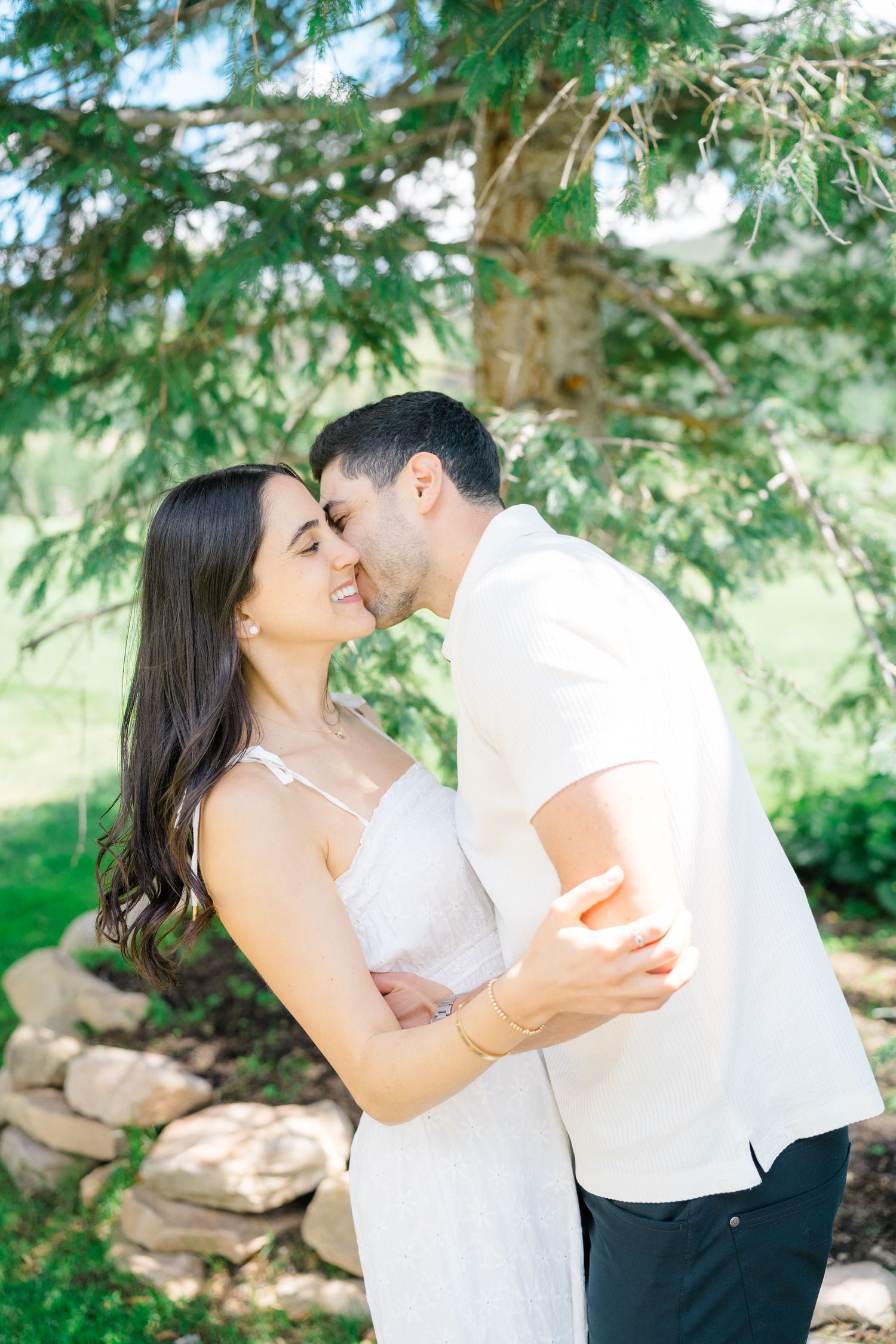 A tender moment shared between a couple under pine trees on a sunny afternoon.