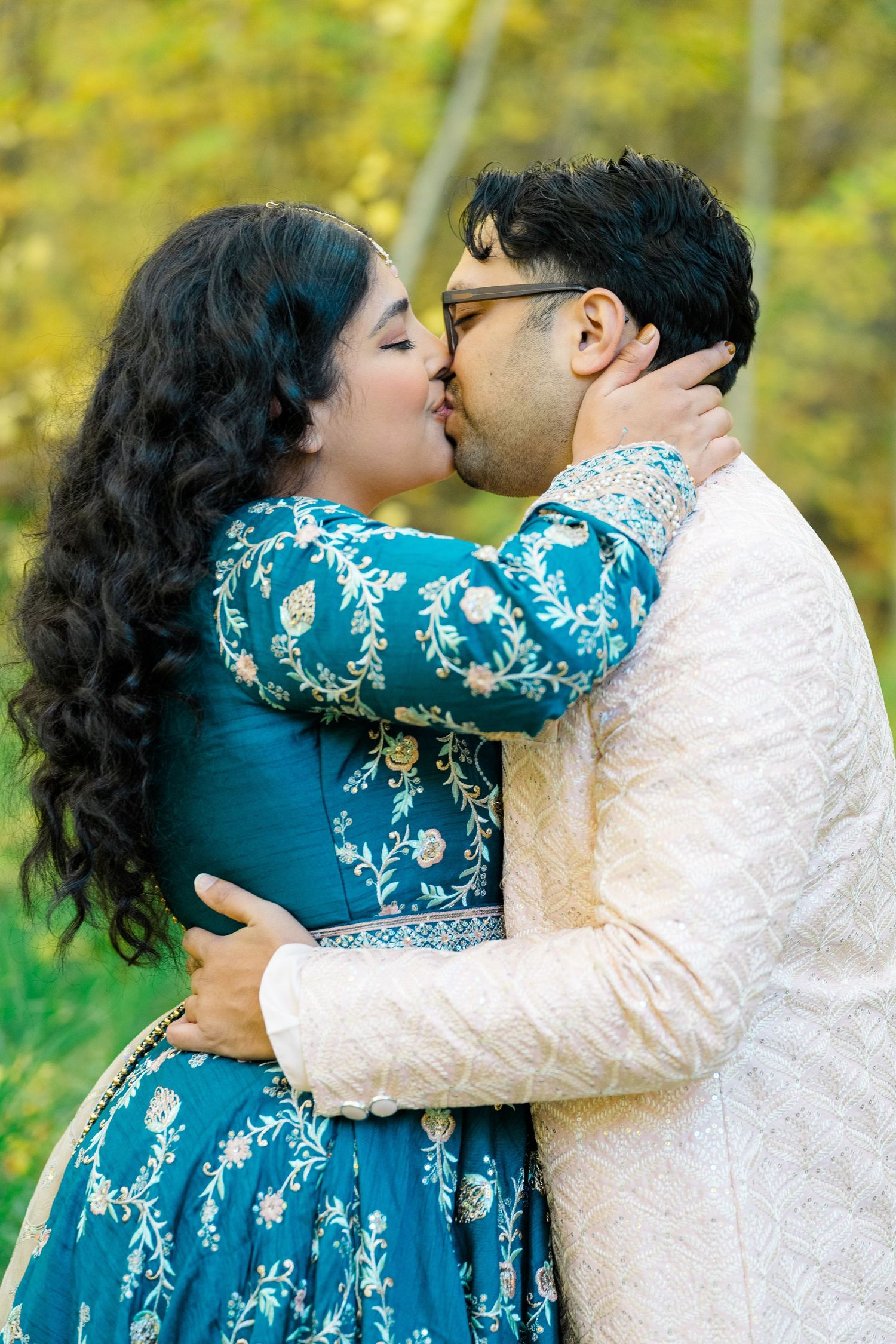 A couple in teal and white traditional outfits share romantic moments in a series of outdoor photos with autumn foliage.