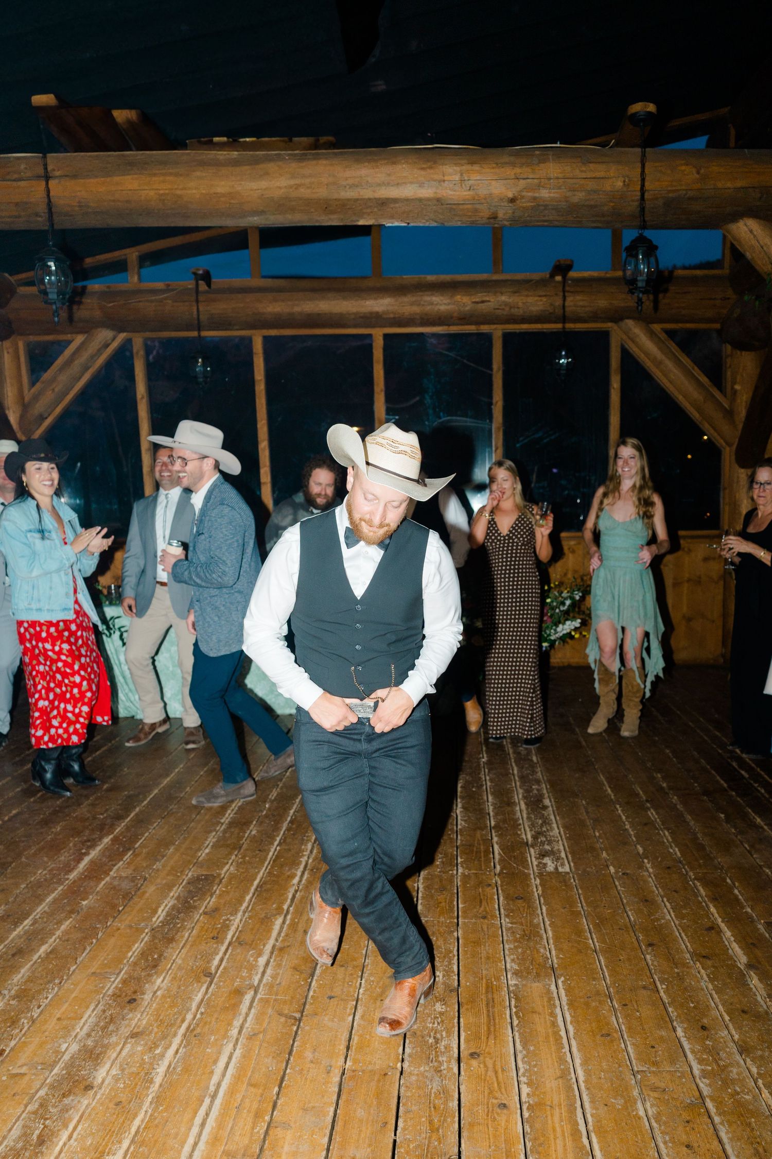 Wedding guests dance on a wooden floor during a lively barn reception celebration.