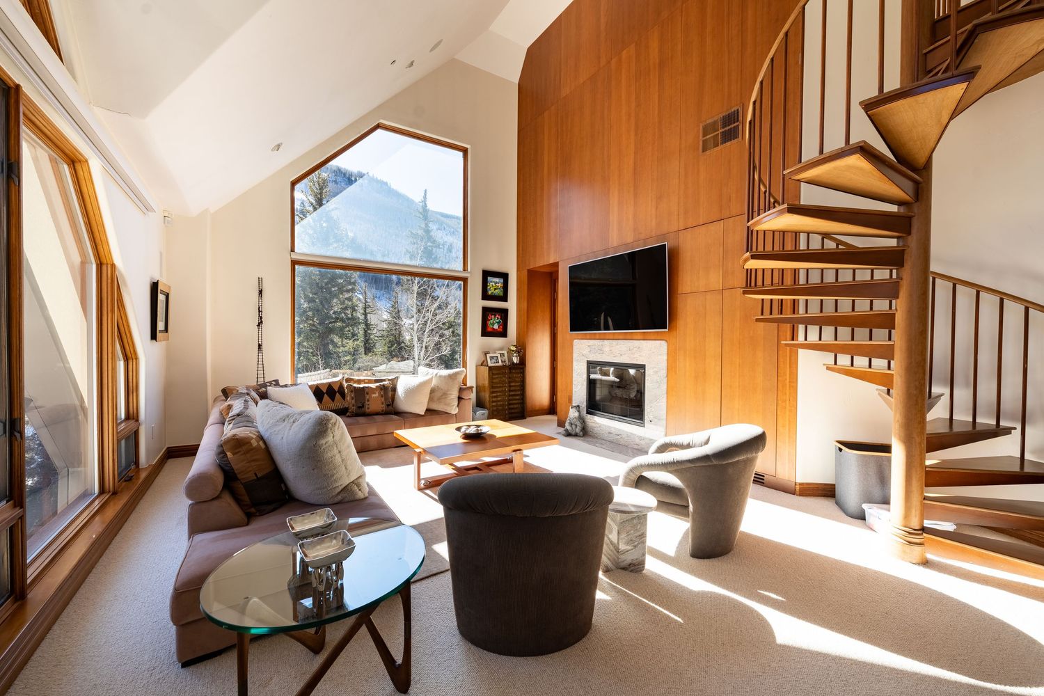 Modern wooden cabin interior with spiral staircase and large windows showcasing mountain views.