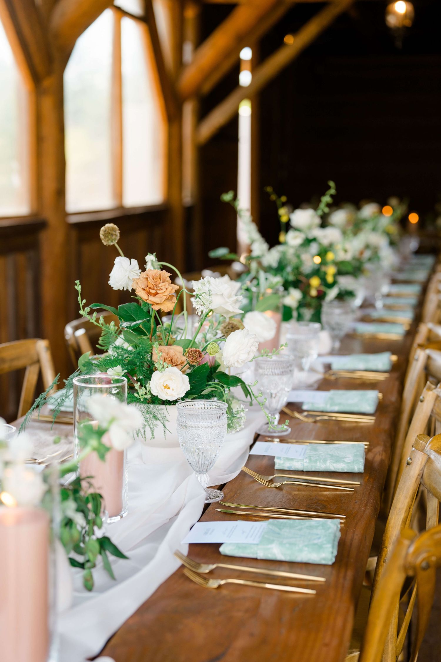 Piney river ranch wedding indoor table with florals and wooden chairs and white drapery.