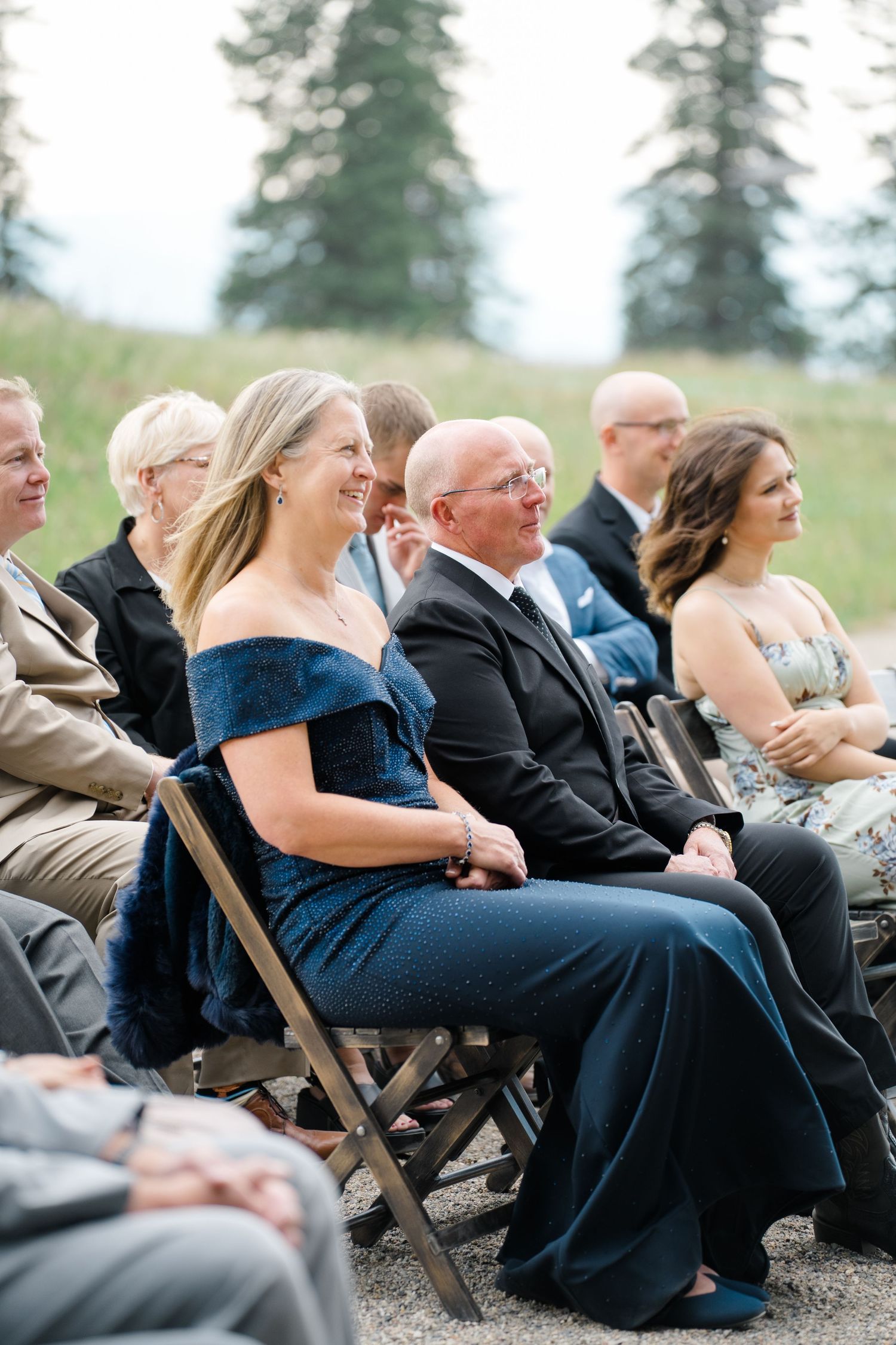 Wedding guests in formal attire sit in wooden folding chairs at an outdoor ceremony at copper mountain.