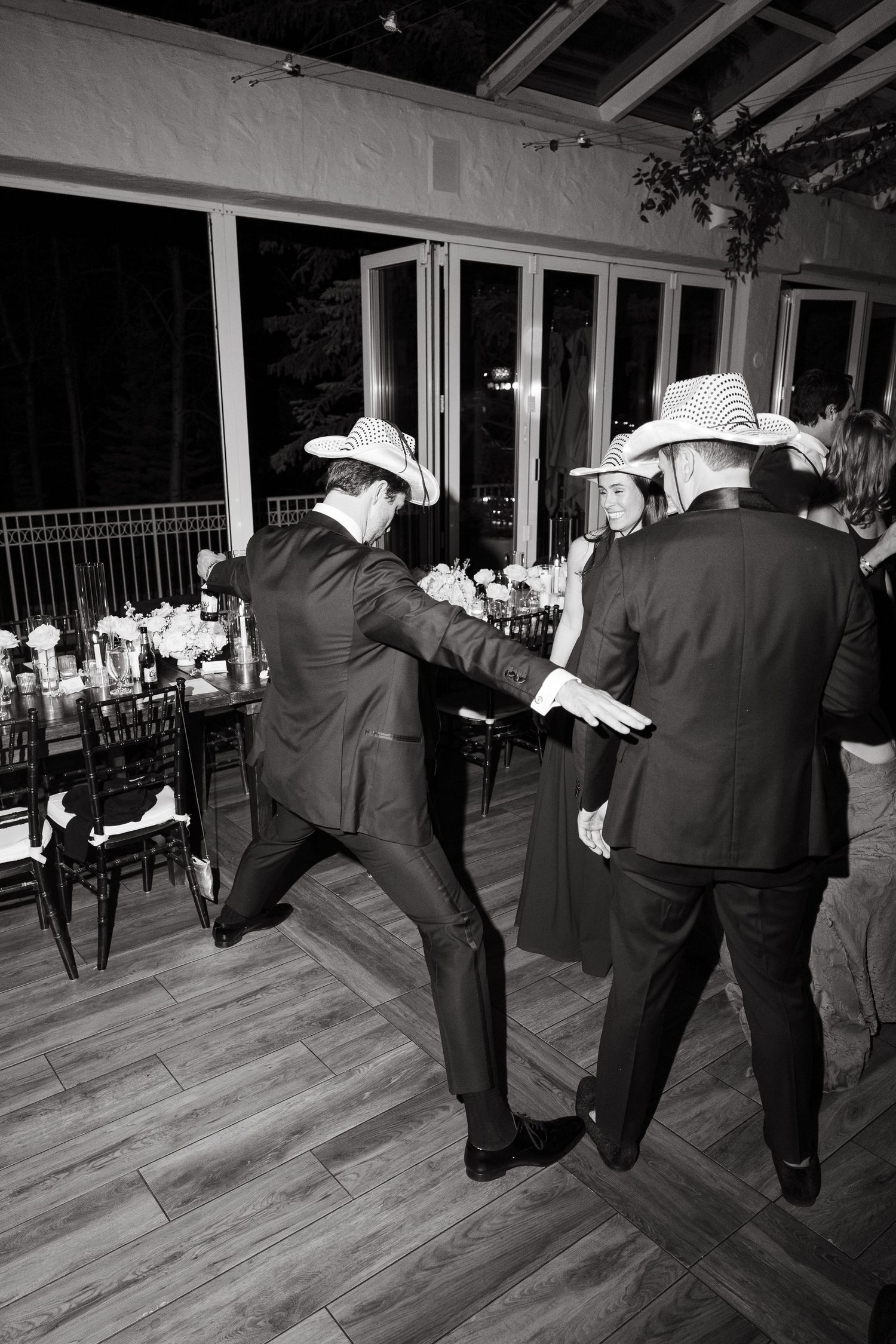 Men in suits and cowboy hats dancing energetically at an indoor wedding reception in black and white photo at Vail Sonnenalp Wedding.