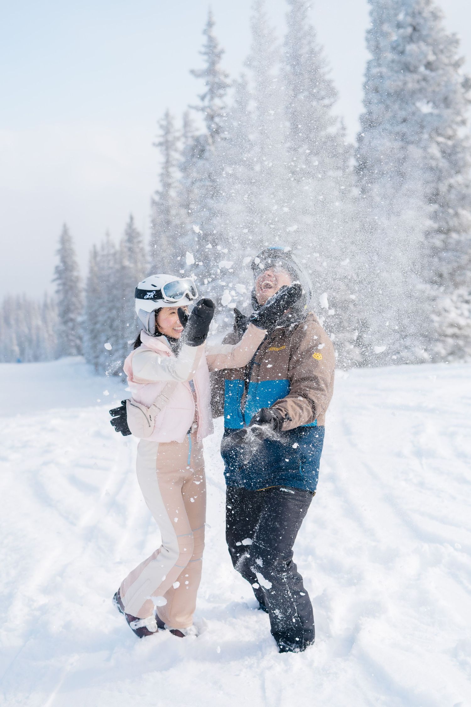 A couple plays in the snow during a winter engagement photoshoot in a snowy forest landscape.