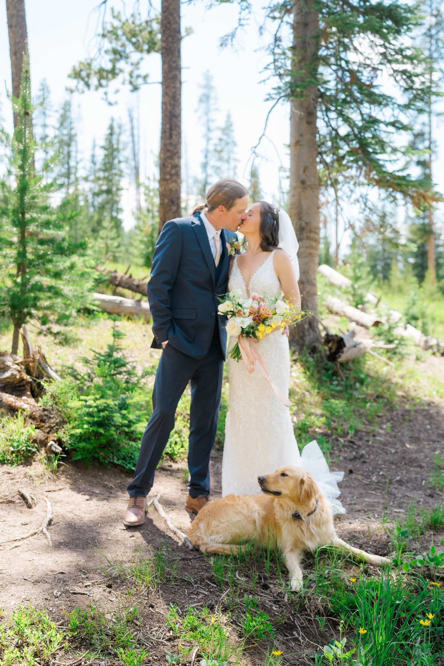 A couple shares a romantic moment in a forest setting with their golden retriever sitting beside them on a nature trail.