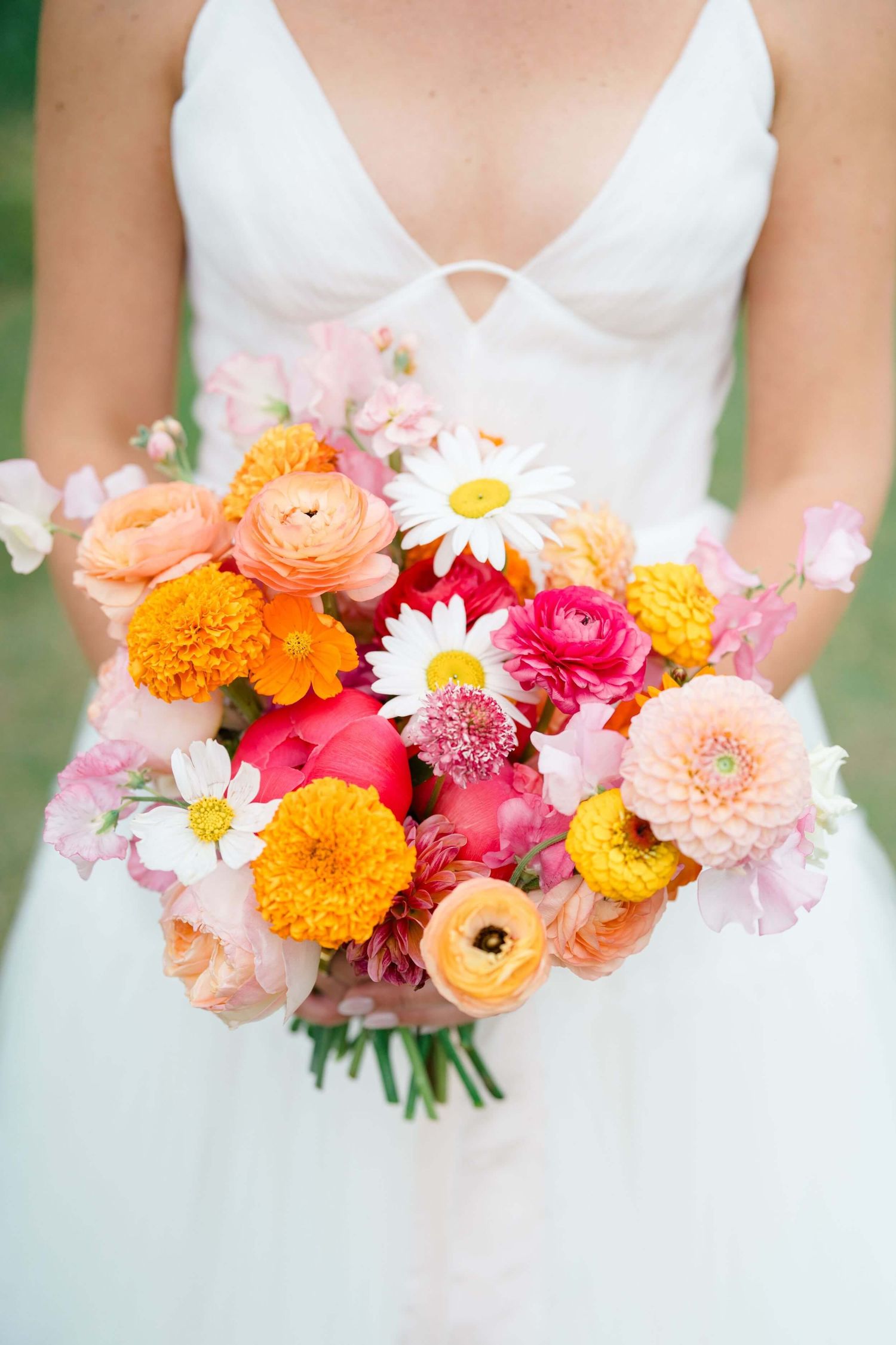 Camp Hale Wedding - Vibrant summer wedding bouquet with orange, pink and white flowers held against a white wedding dress.